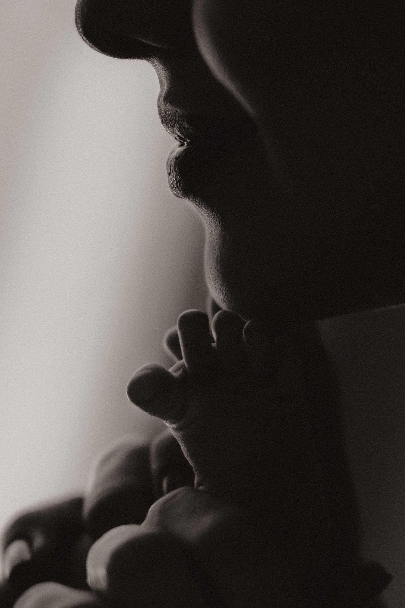 Parent kissing their newborn’s tiny feet in soft light during an intimate lifestyle moment.