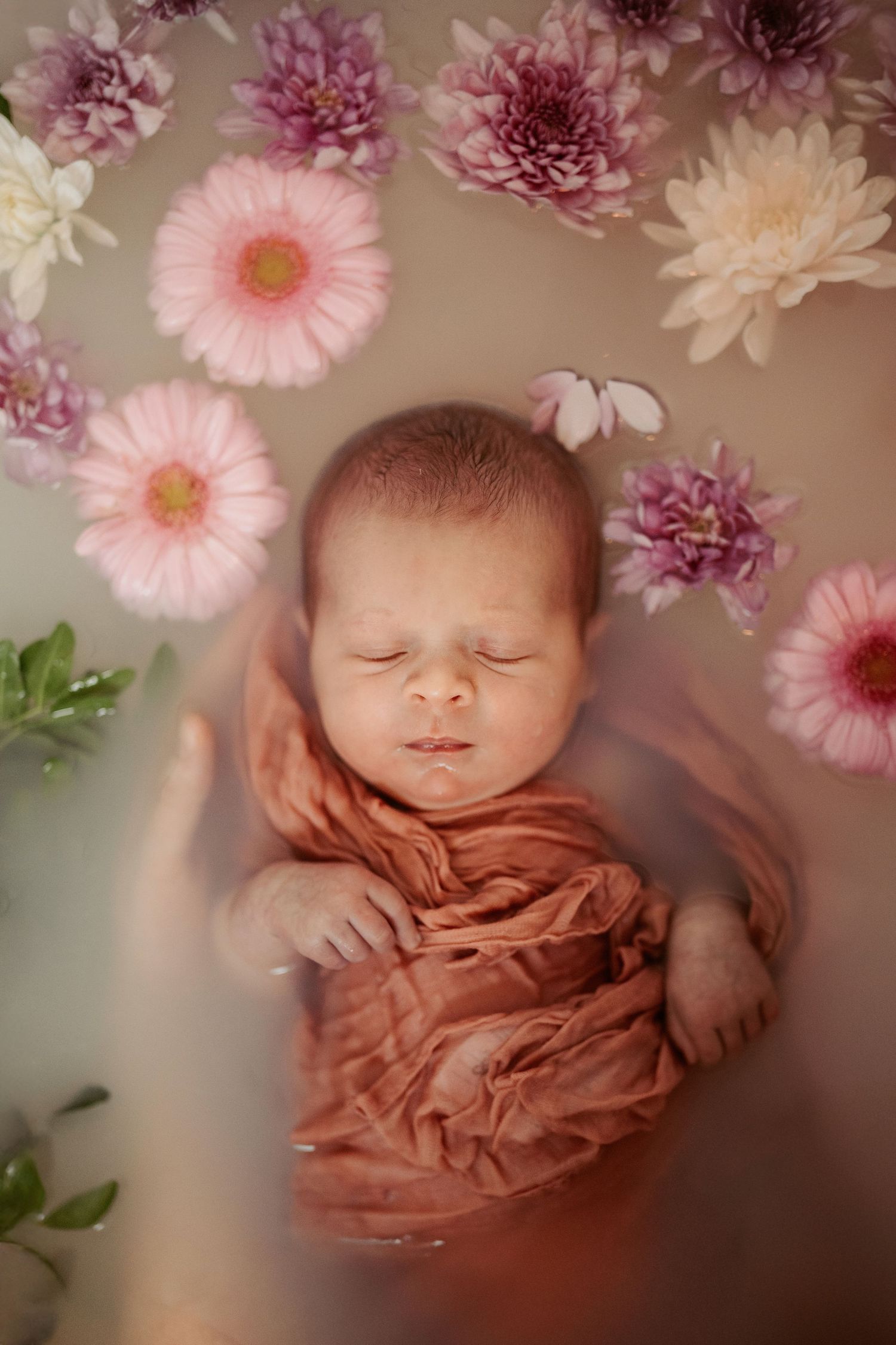 Newborn lying in a floral milk bath during a creative newborn photography session with soft natural light in Asby de la Zouch