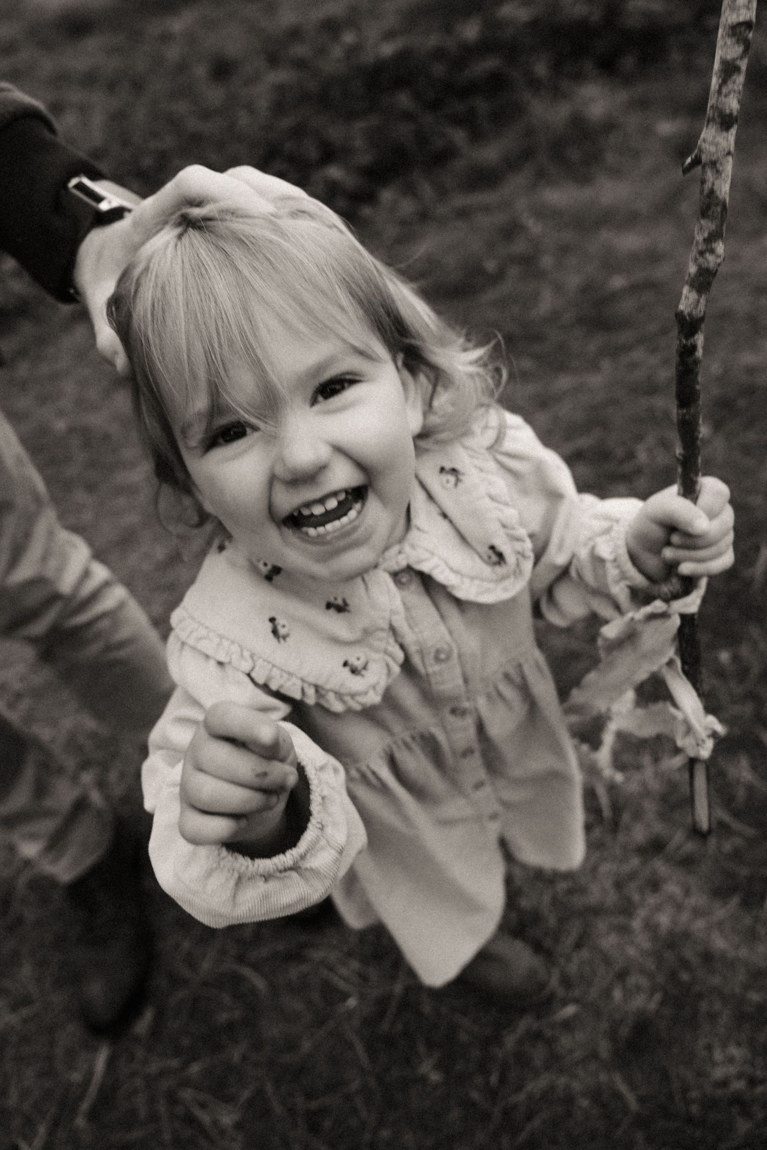 Little girl laughs while holding a stick during a candid outdoor childhood photography session.