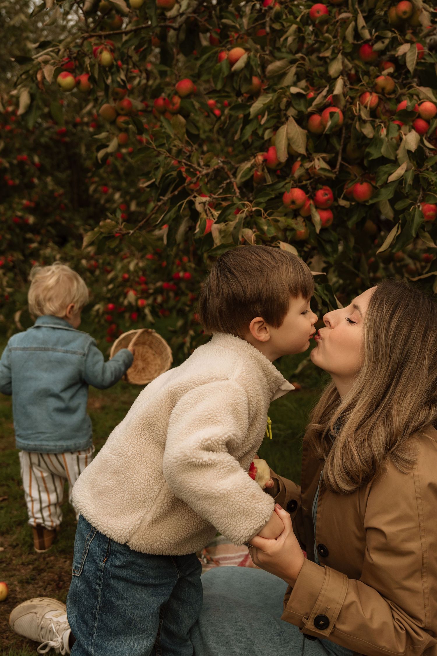 Little boy rests his head on his dad’s shoulder during a warm autumn apple orchard photoshoot.