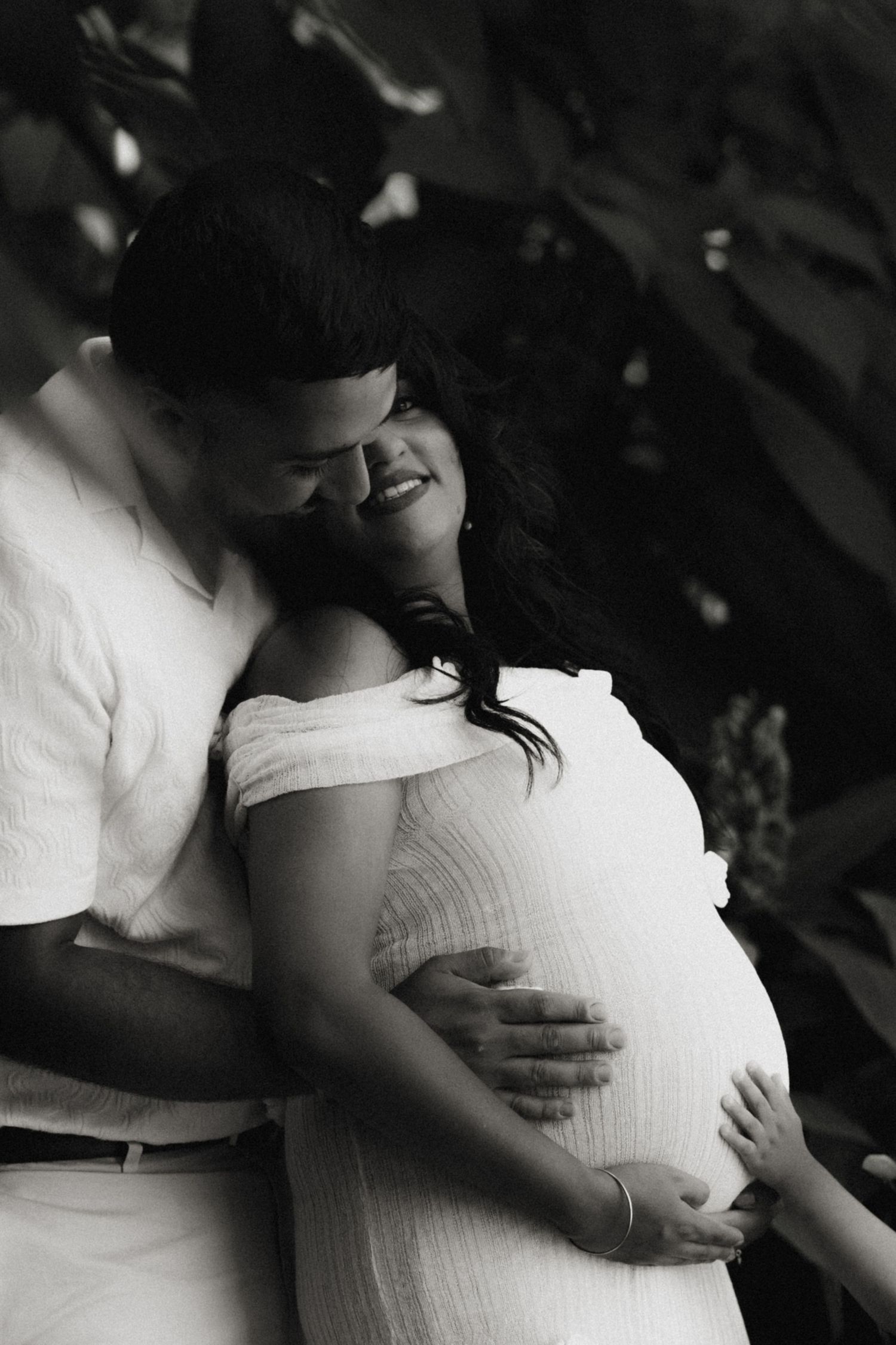 Expectant parents embracing, one hand resting on a pregnant belly, surrounded by soft light and a sense of anticipation