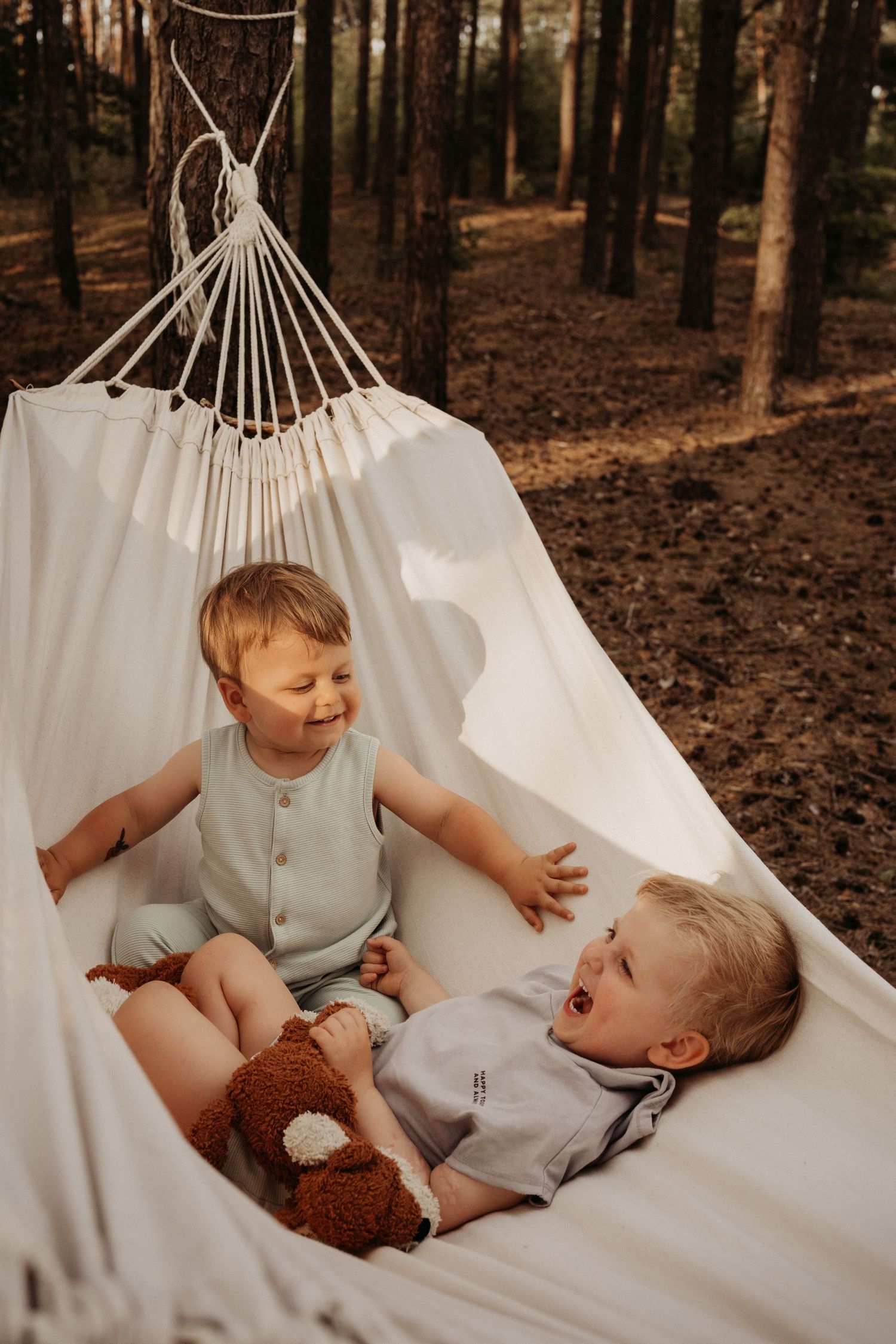 Two little boys relax together in a white hammock during a playful woodland photoshoot in Swadlincote.