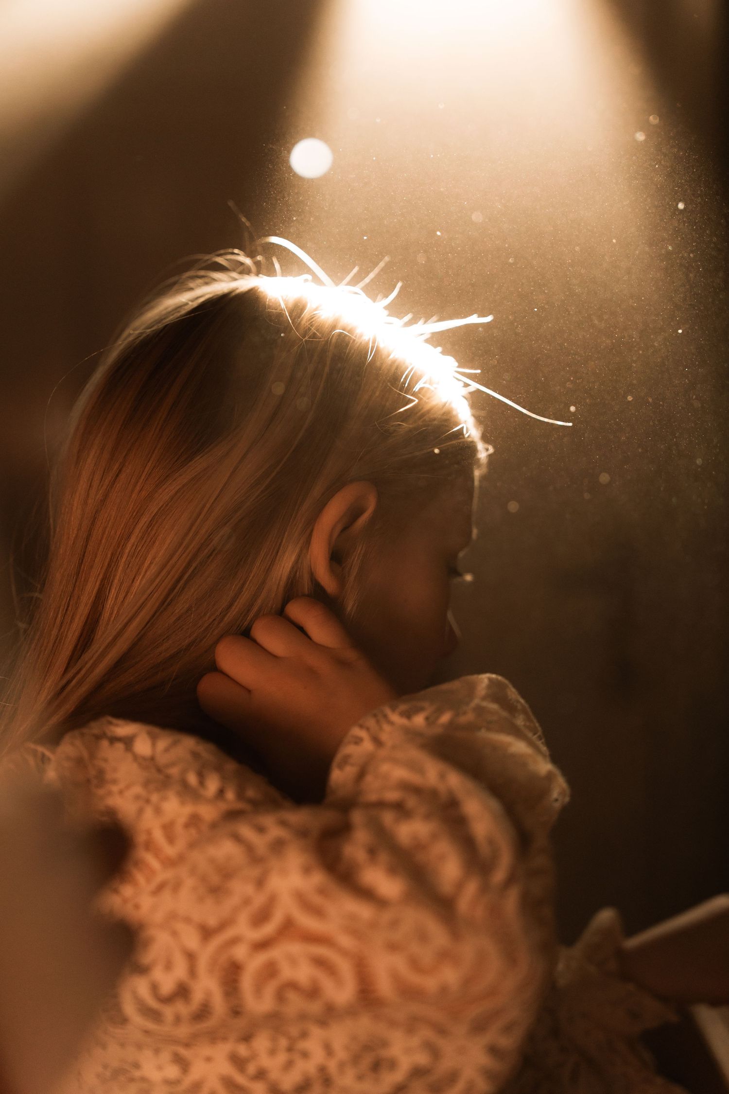 Girl looks through a window with golden light on her hair during a soft storytelling photoshoot in Swadlincote