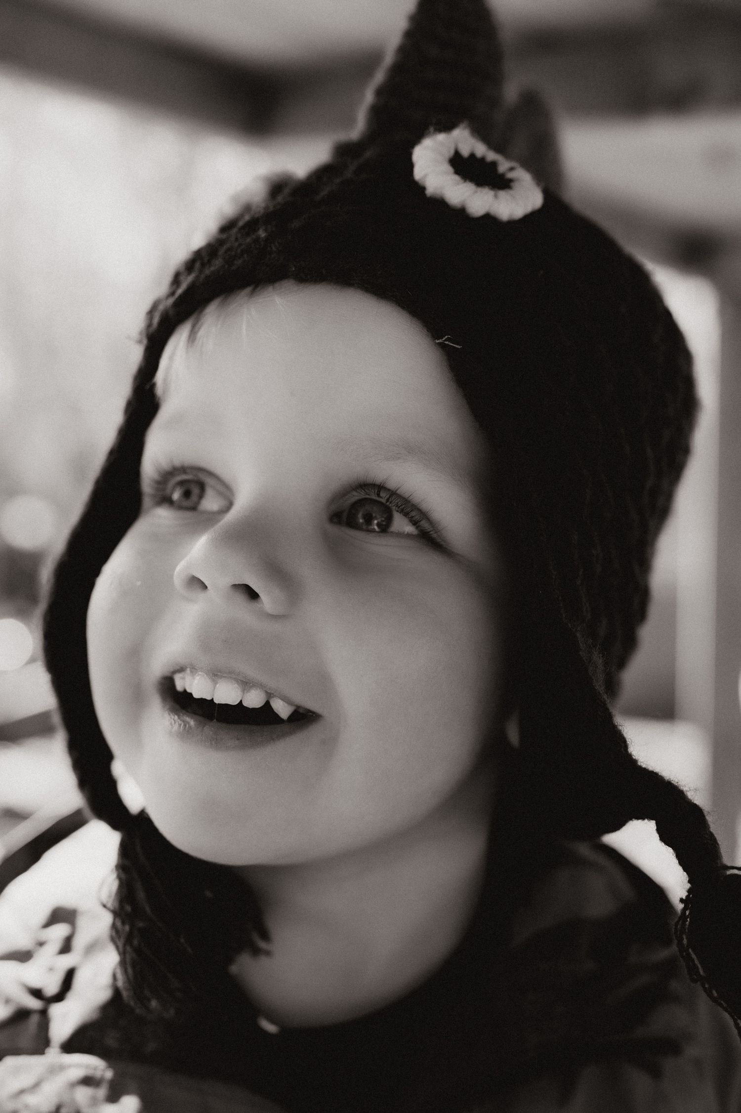 Smiling child in a knitted animal hat looks up, light catching their eyes in black and white, during Little Wildlings Photoshoot