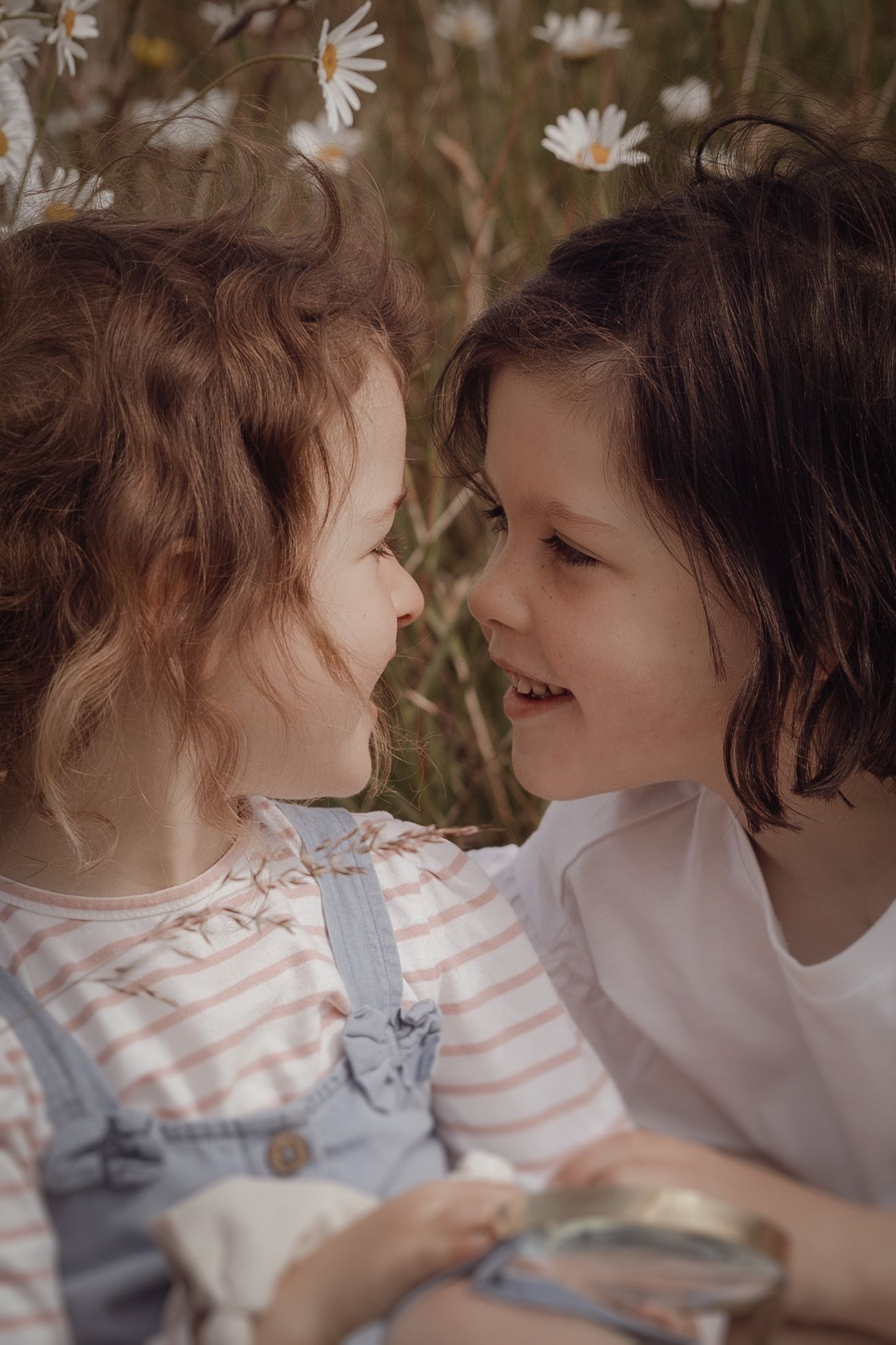 sisters looking closly at each other during a photoshoot in Daisy Field in Swadlincote