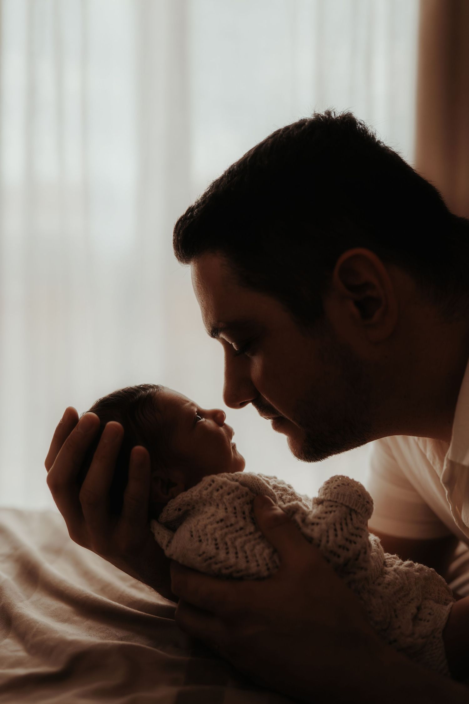 Father leaning in to kiss his newborn during a tender storytelling newborn photoshoot by the window in Ashby