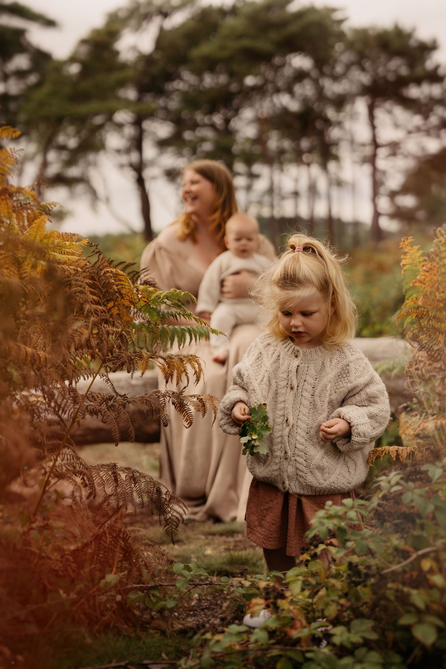 Mum sitting on a fallen tree with her son, older daughter exploring freely the autumnal surrounding