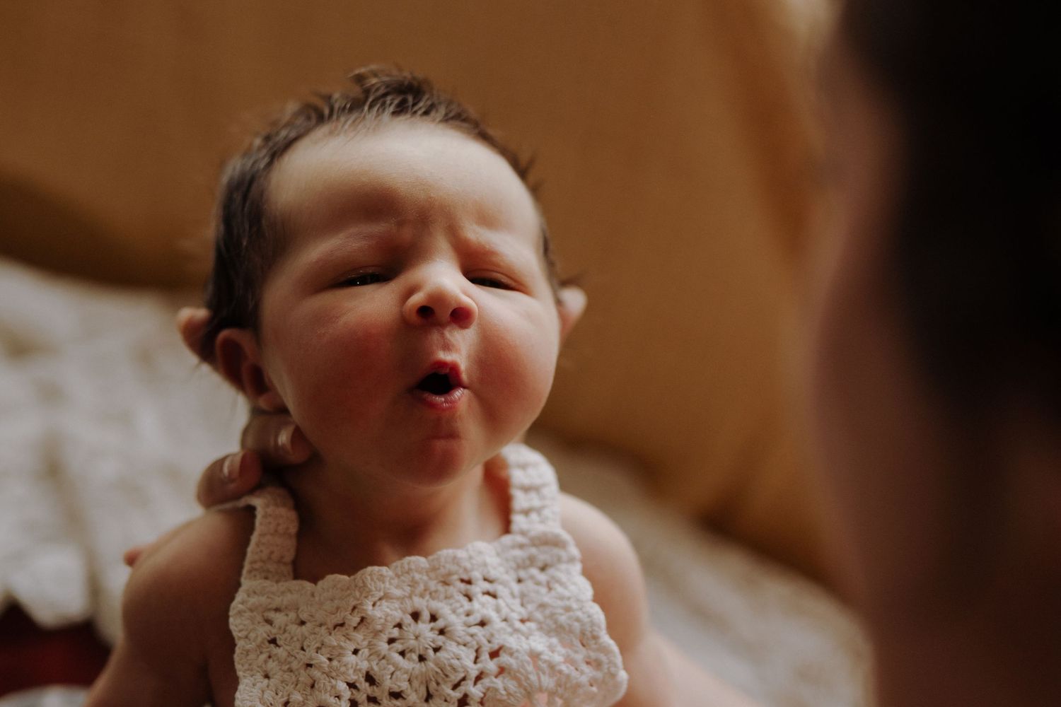 Newborn baby in a crochet outfit makes an adorable face during an at-home lifestyle session in Melbourne