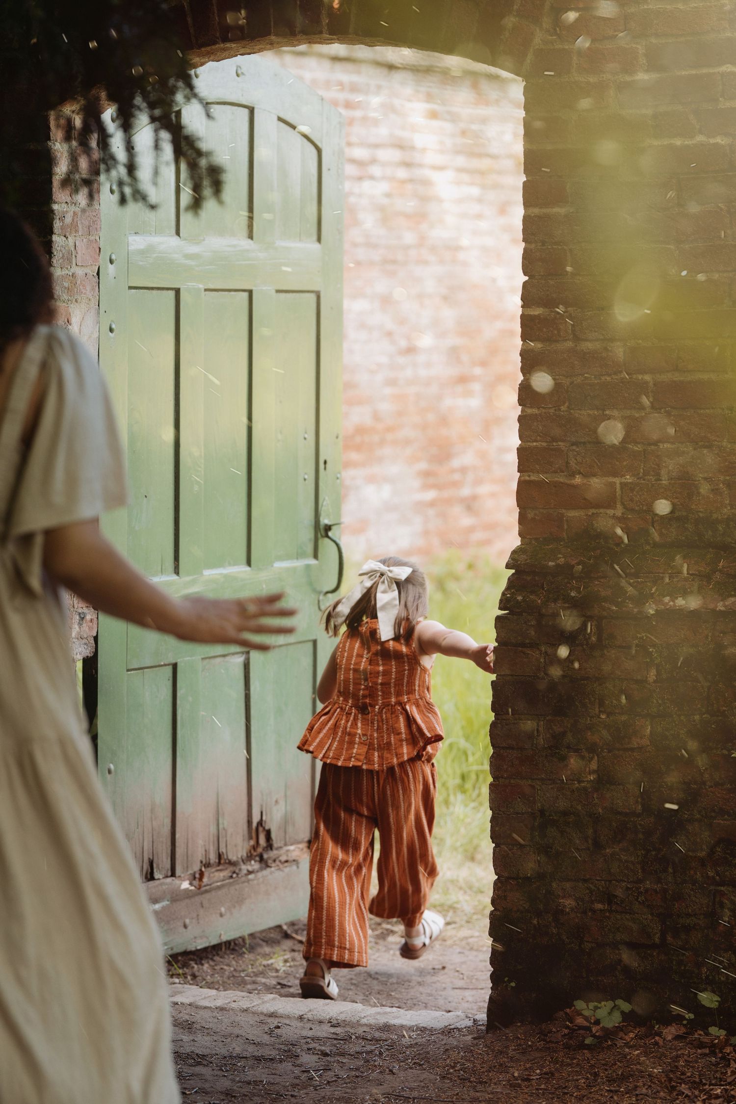 Girl in rust-coloured outfit walks through a brick archway during a natural family and maternity photoshoot in Midlands