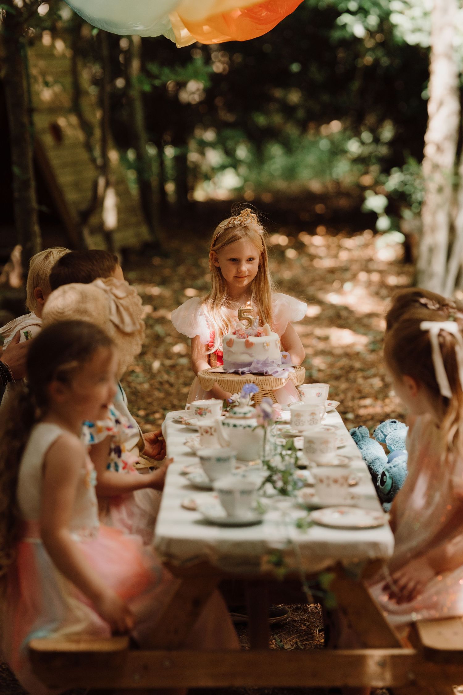Children gathered around a decorated table outdoors during a whimsical birthday tea party at Little Wildlings Nature Play