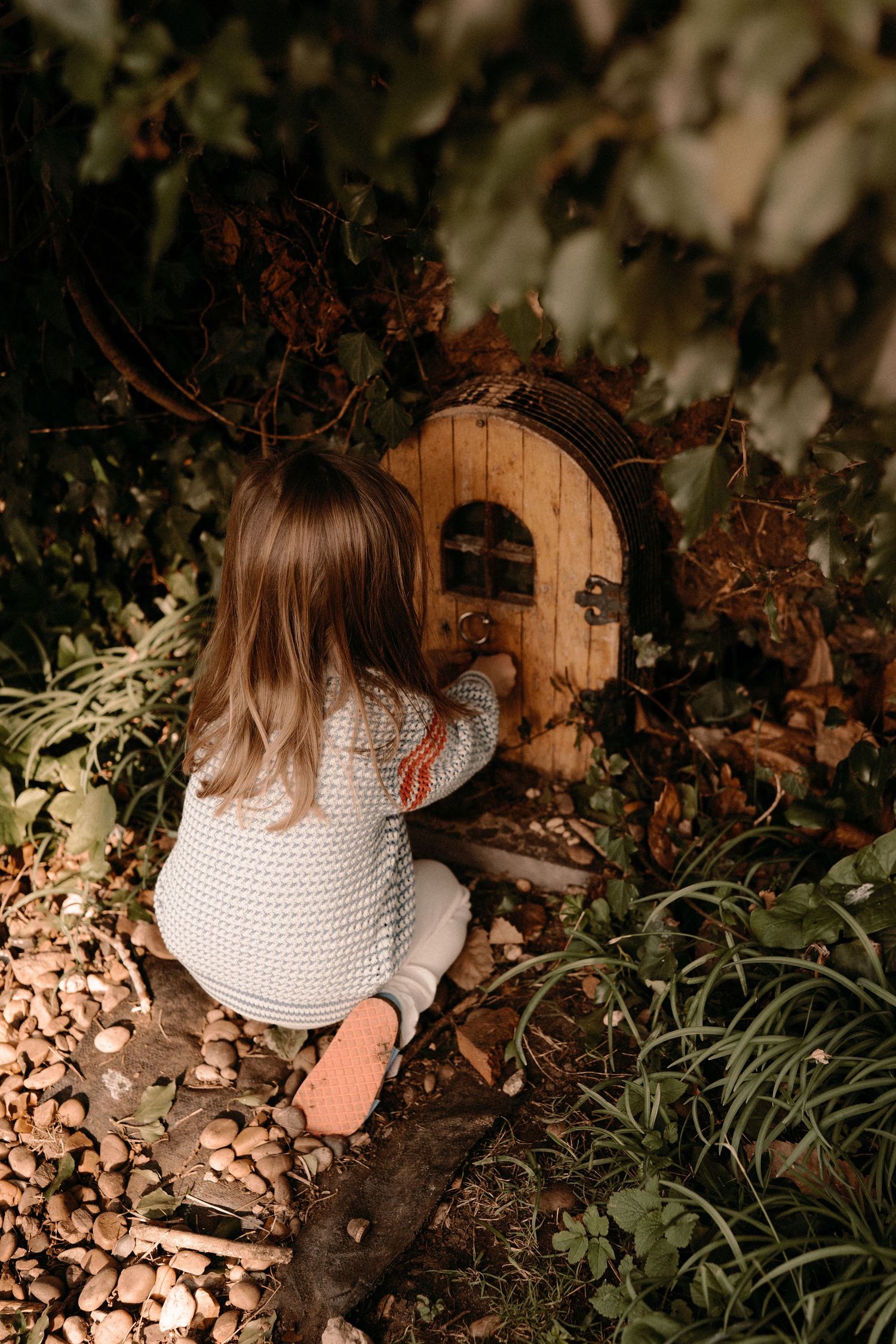 Little girl explores a tiny wooden fairy door during a magical childhood photography session in Tamworth