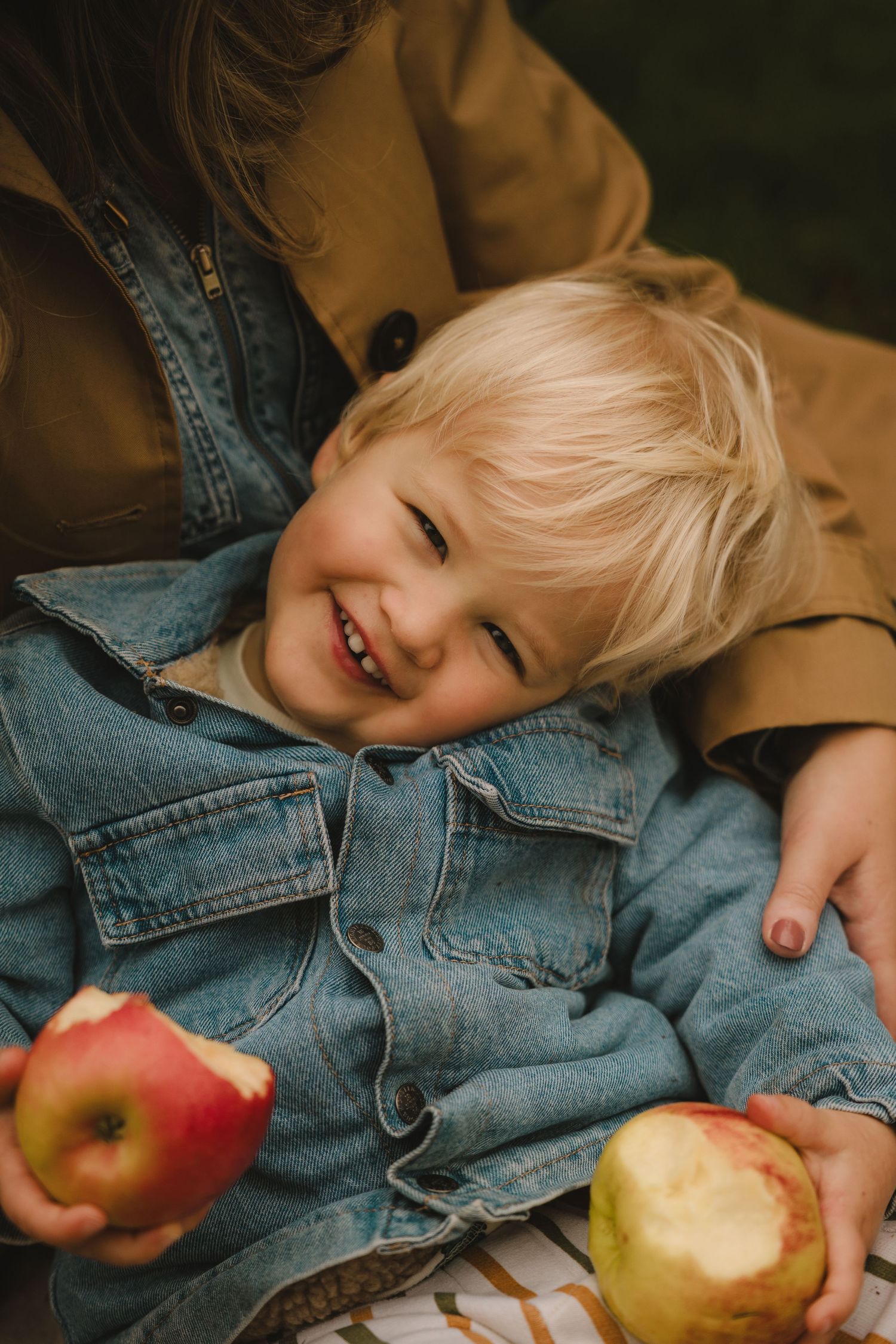 Smiling boy in denim jacket holds apples during a cozy autumn family photoshoot in Tamworth