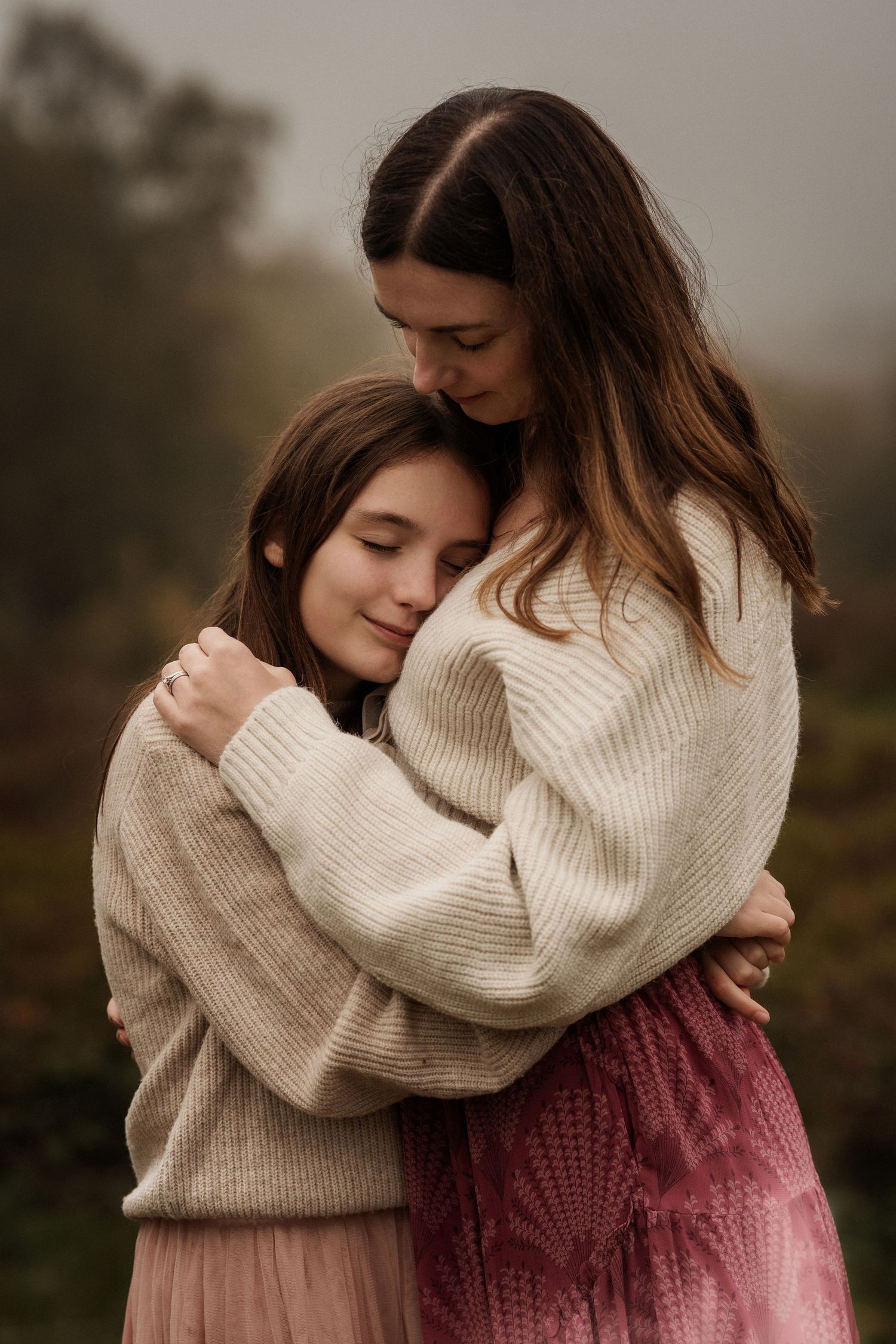 Mother and daughter share a quiet hug in soft light during an emotional outdoor family session in Lickey Hills