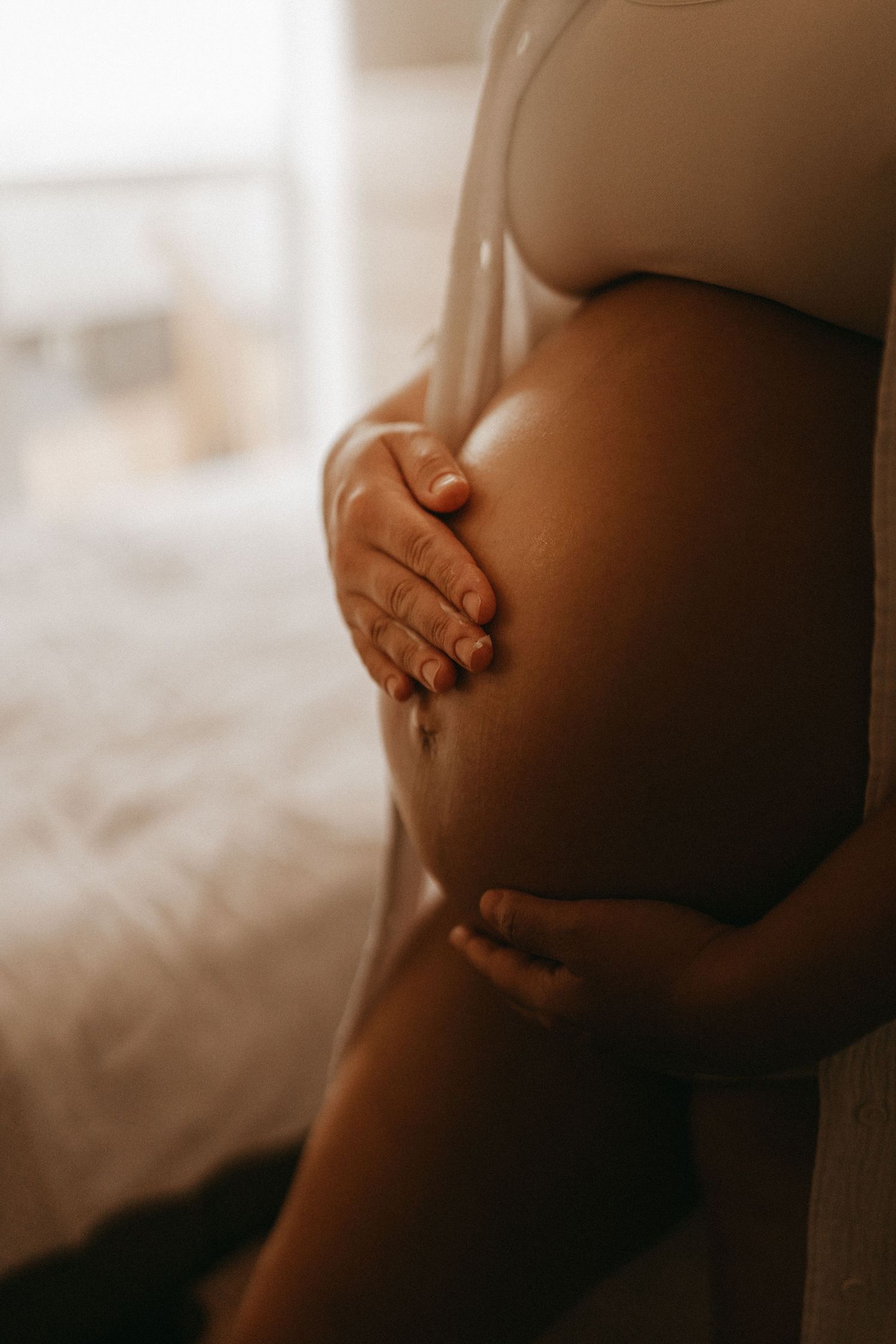 Hands holding a bare pregnant belly in warm natural light during an intimate maternity session in Stoke on Trent