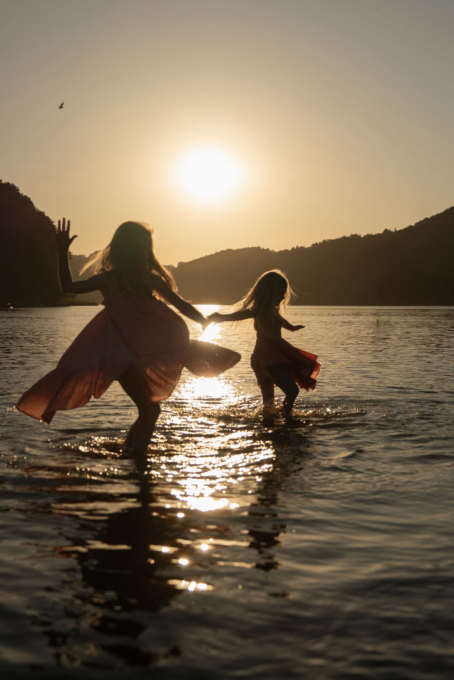 Two girls playing in the water at sunset, captured in warm cinematic light during a lifestyle family photography session.
