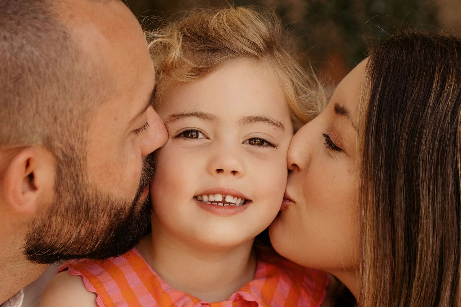 Parents kiss their daughter’s cheeks during a golden-hour family storytelling photoshoot.