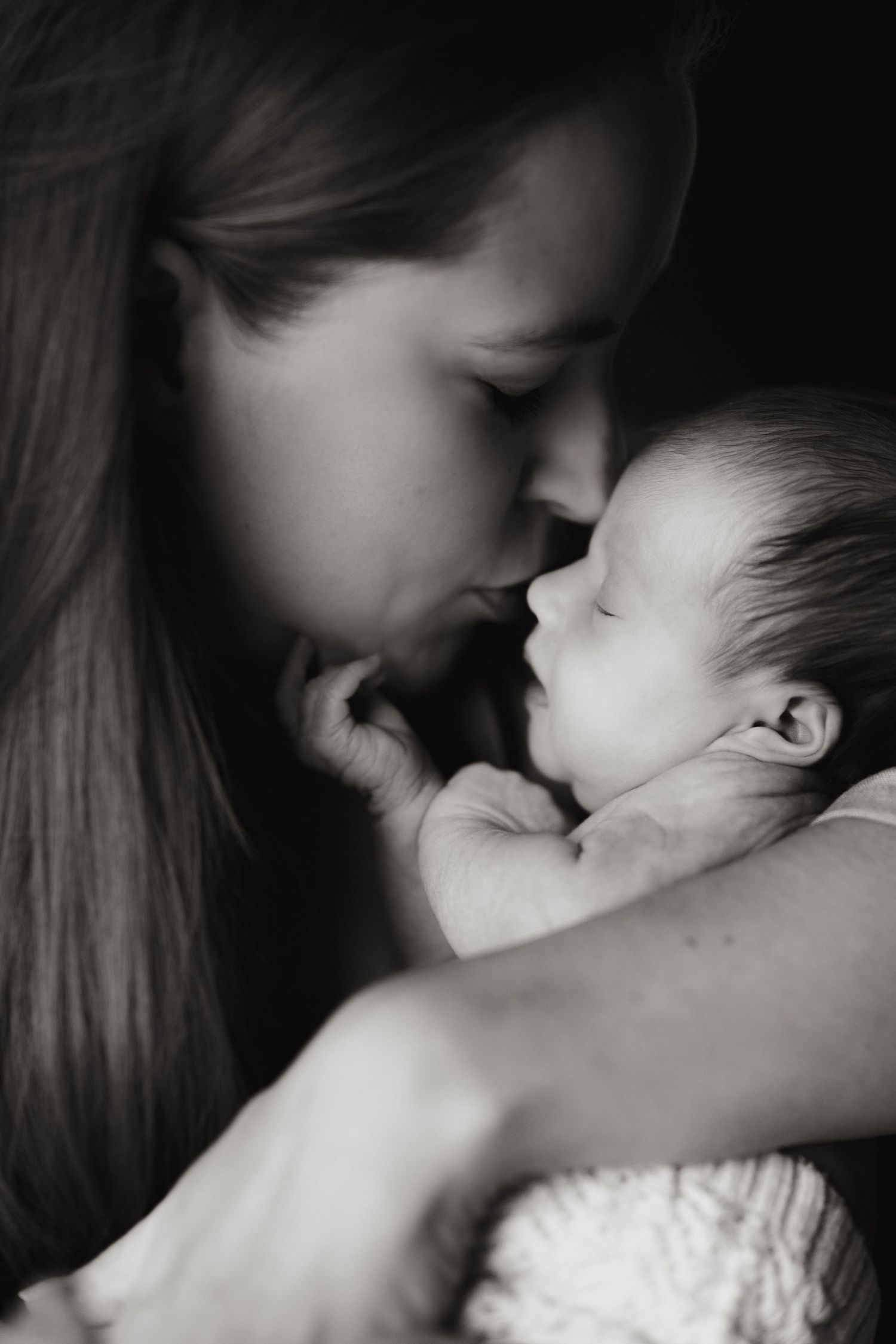 Mother kissing her newborn during an intimate storytelling newborn photoshoot in black and white.