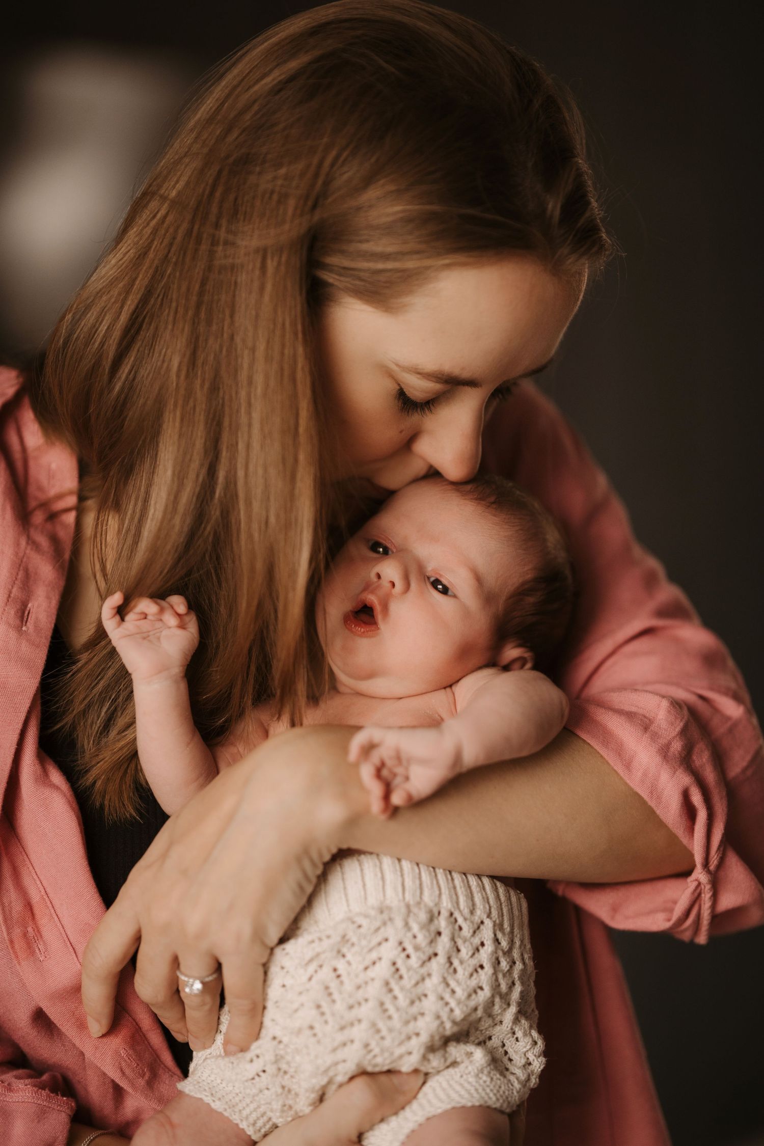 Mother kissing her newborn during a tender storytelling newborn photoshoot in soft light in Swadlincote