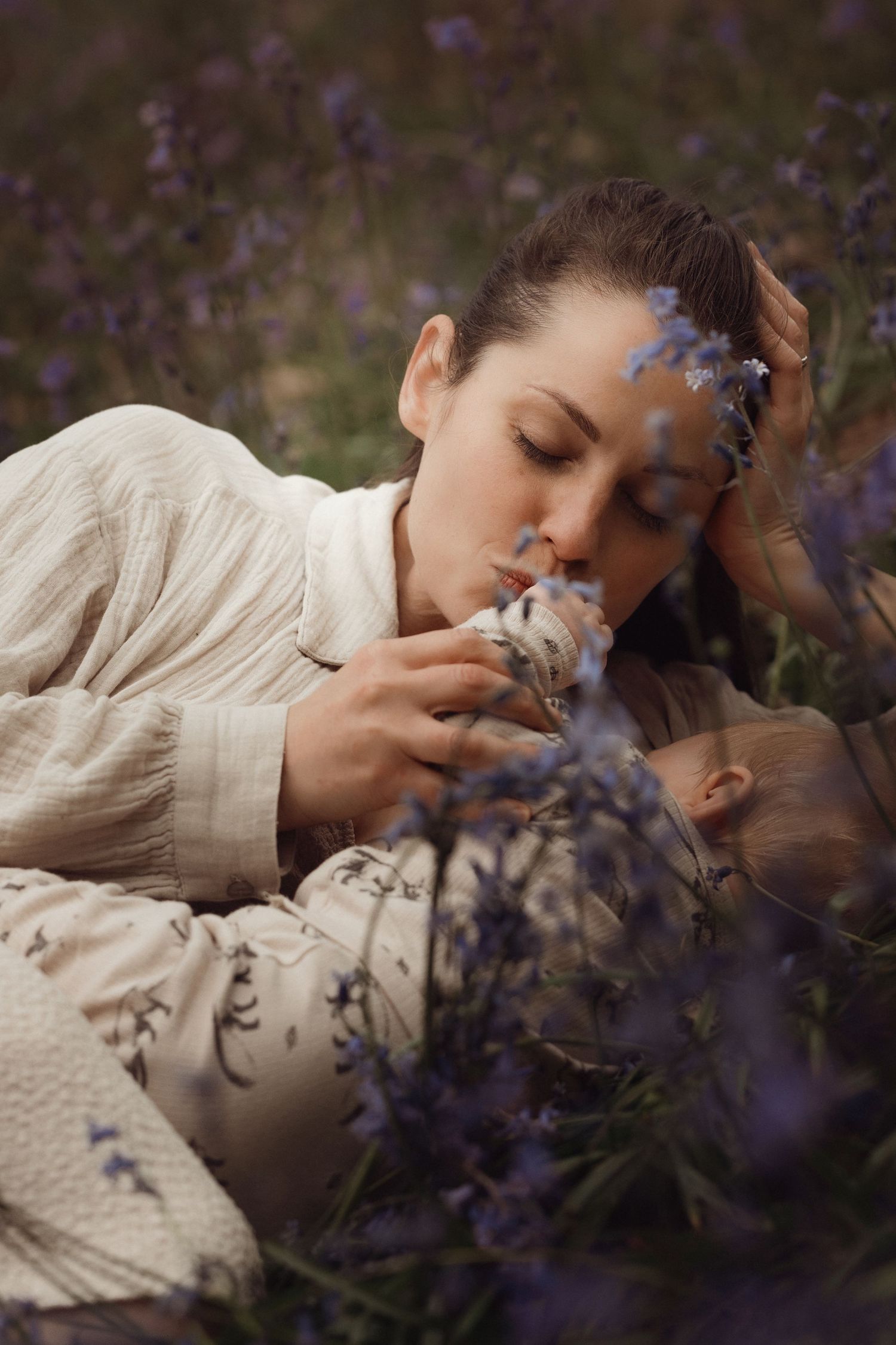 Mother breastfeeding her baby in a flower field during a gentle outdoor documentary motherhood photoshoot in bluebells