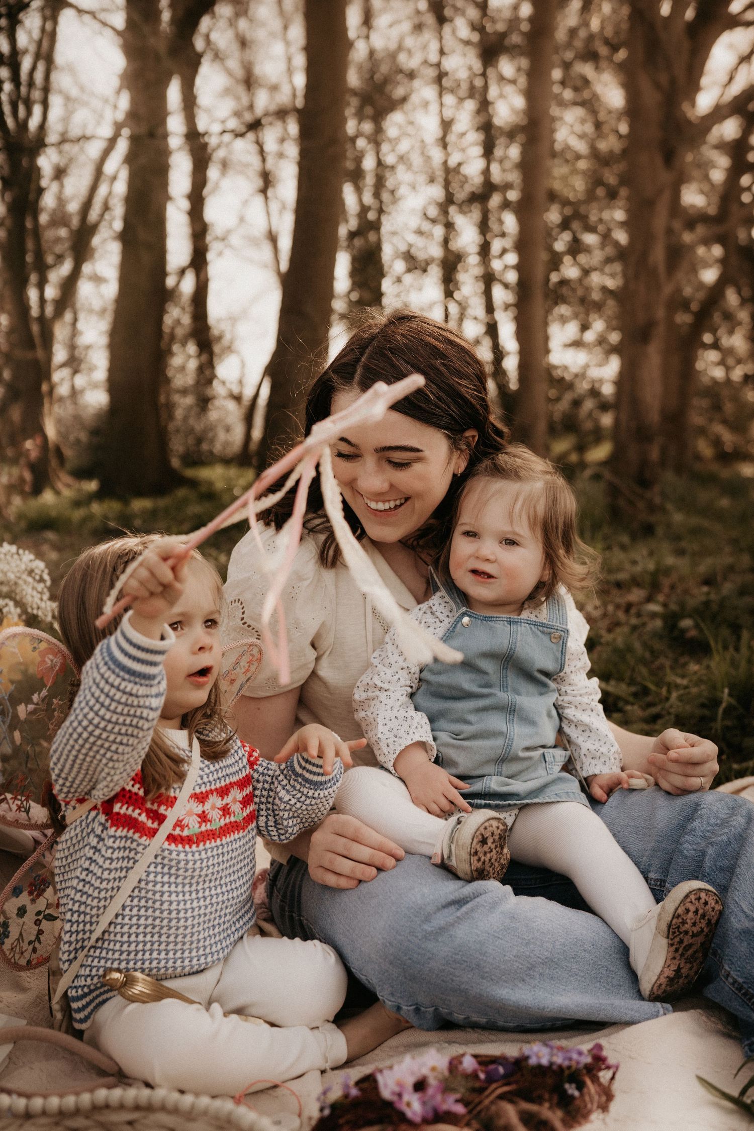 Mother sits with two daughters during a cozy outdoor family photoshoot in Tamworth woodland.