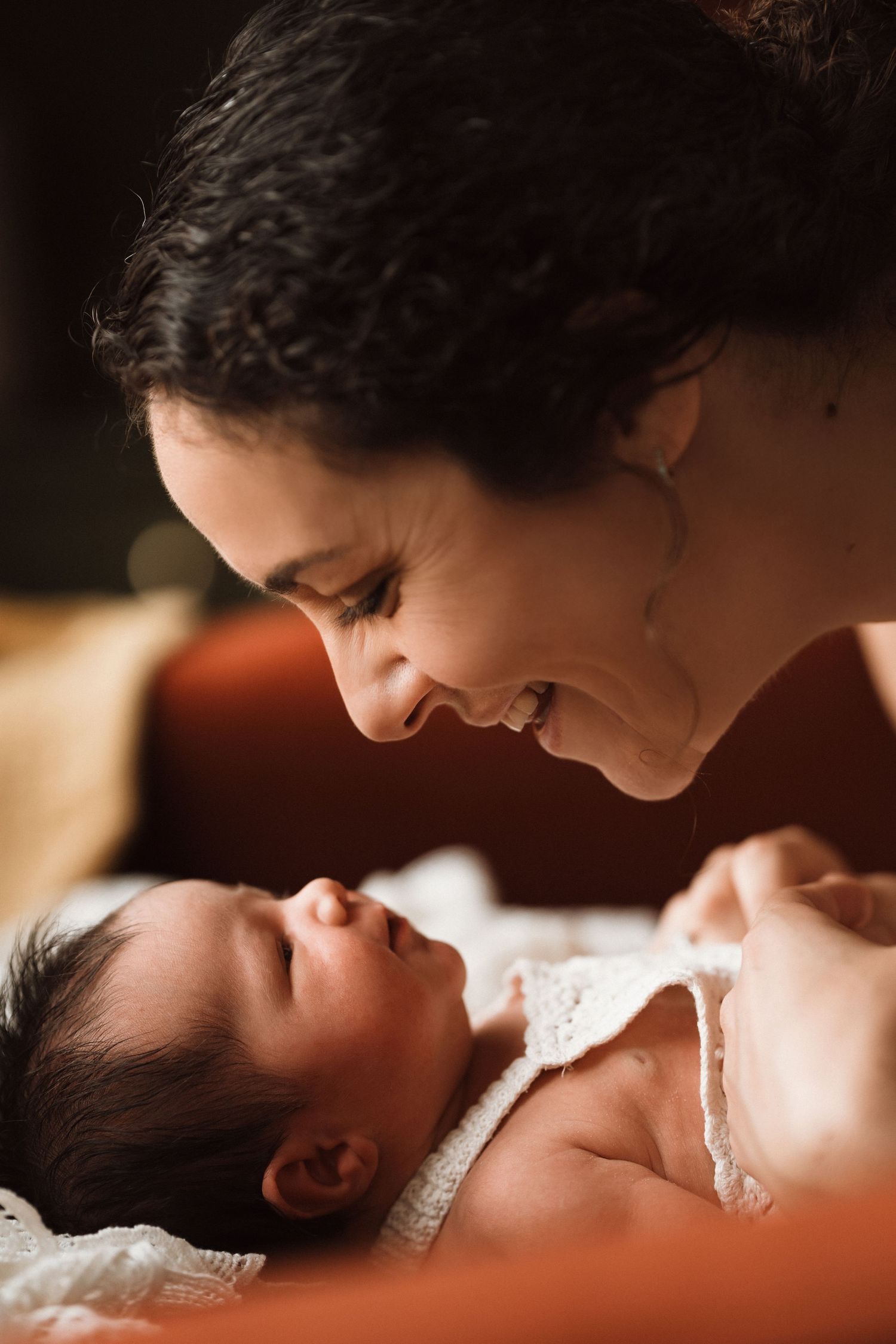 Mum gazes lovingly at her newborn, smiling softly during a warm and emotional bonding moment.