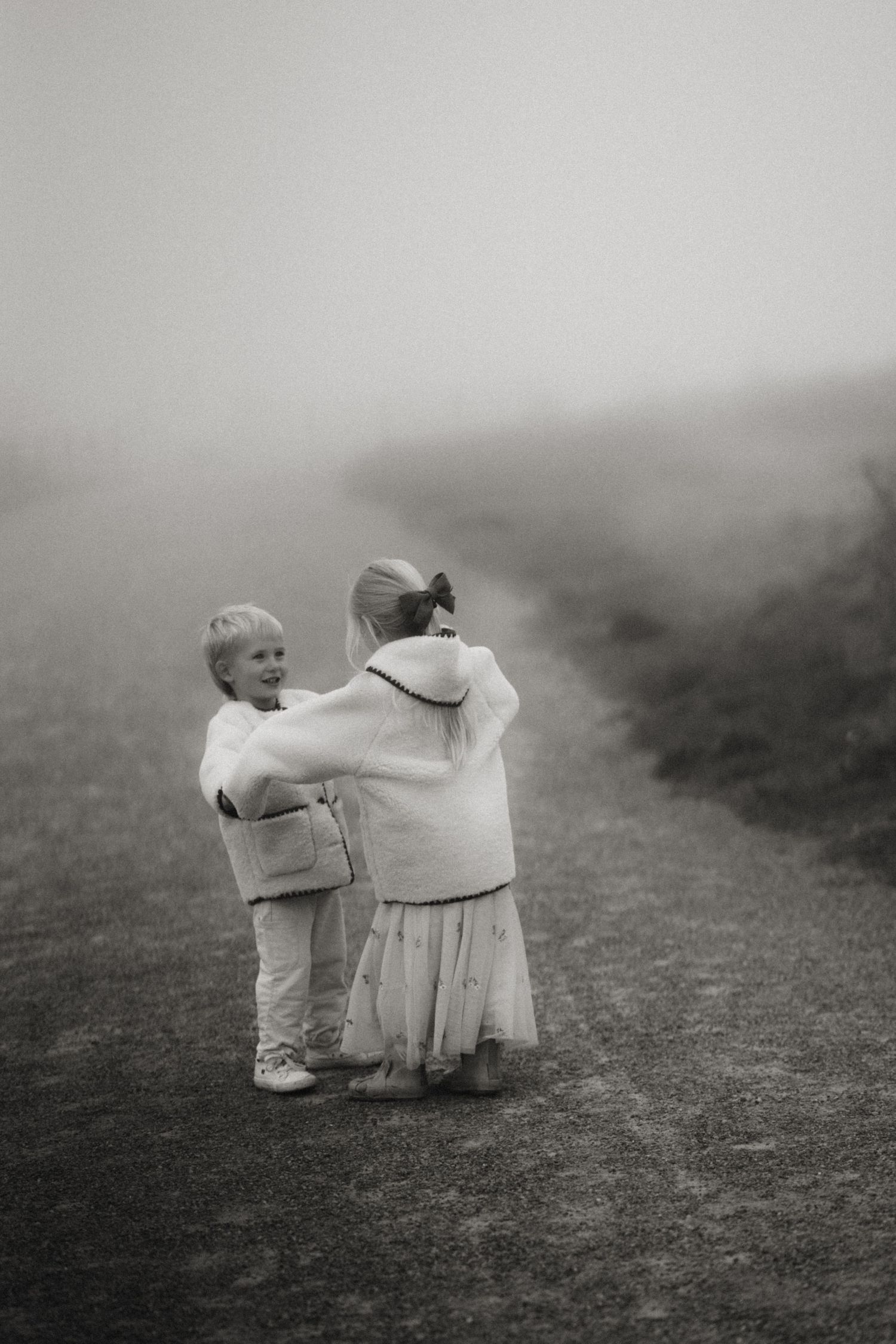 Two children embrace on a misty path during a heartfelt outdoor family photoshoot in the Midlands, Swadlincote