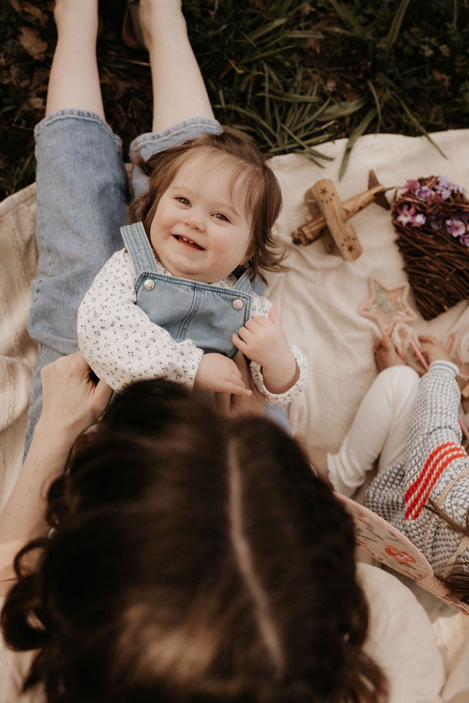Toddler laughs while lying on a blanket during a playful spring family storytelling session.
