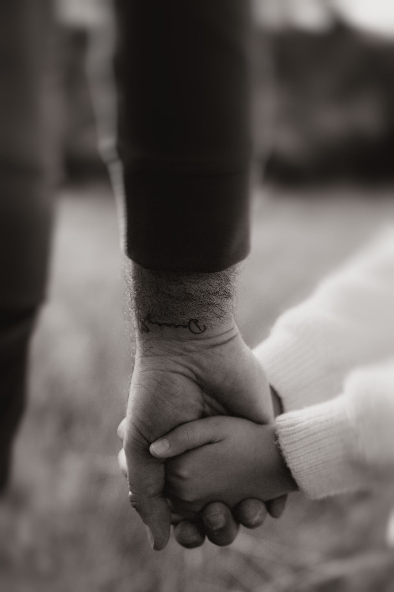 Dads and daughter's hands intertwined, symbolising love and connection during an outdoor family session.