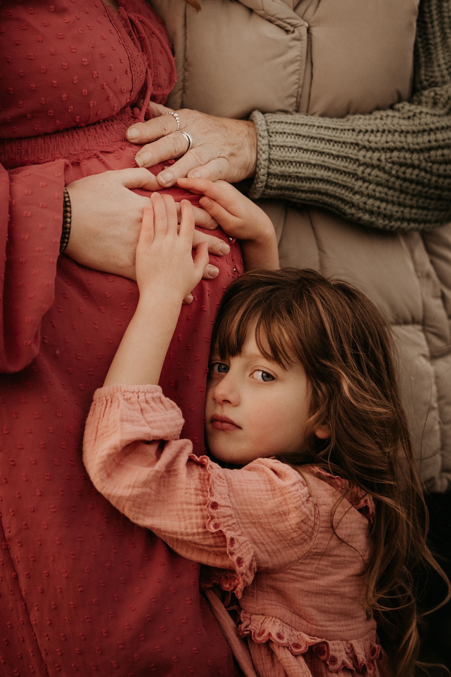 Close-up of hands resting on a baby bump, three generations - grandmother, pregnant mother and her daughter