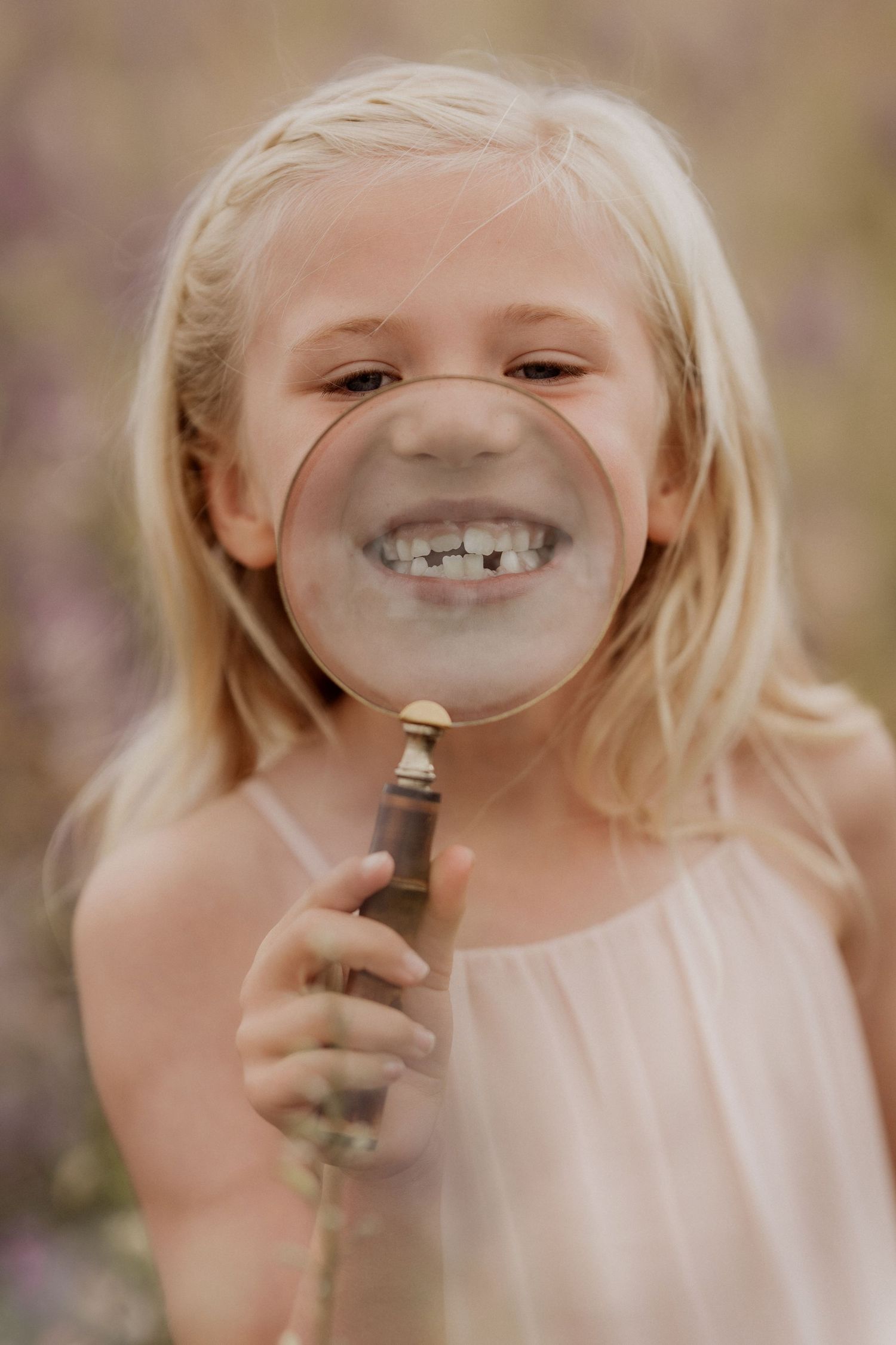 Child smiling while holding a magnifying glass in front of their face during a confetti field mini photoshoot