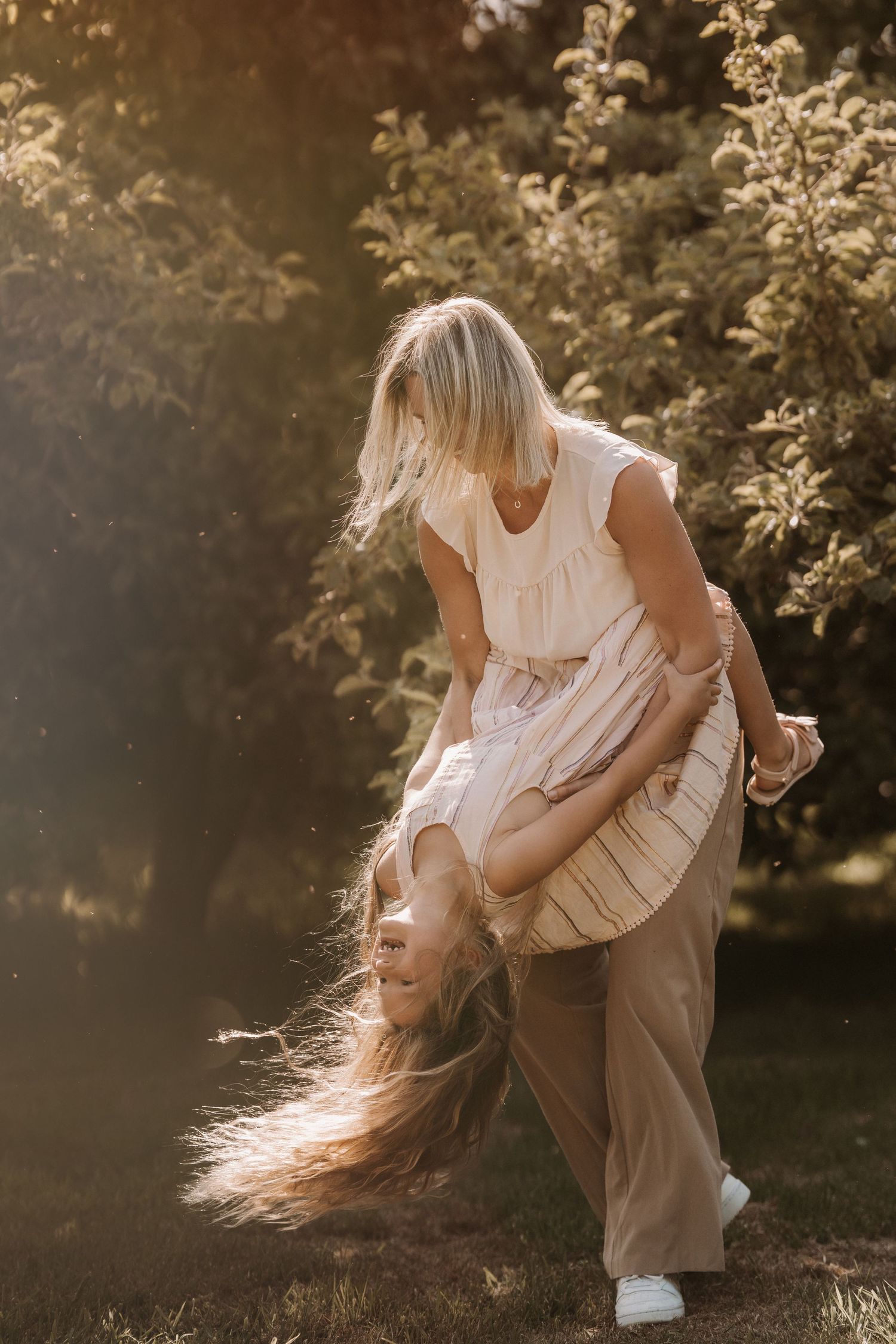 Parent holding a young child outdoors, walking through sunlight with trees in the background.