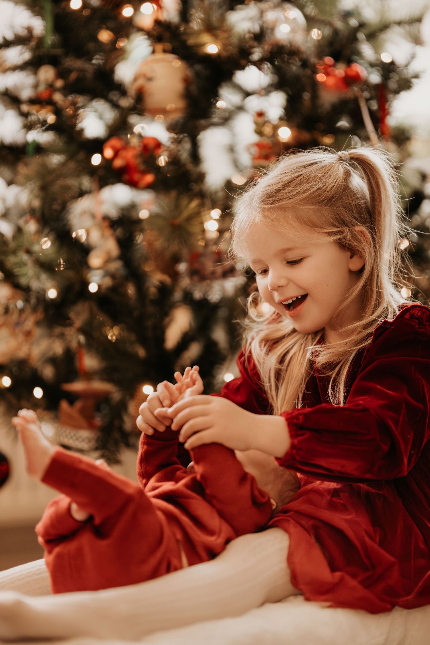 Child playing by a Christmas tree during a cosy lifestyle newborn photoshoot at home in woodville