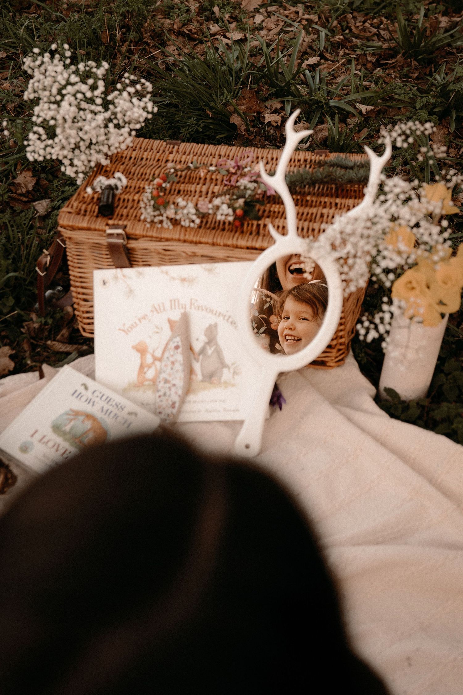 Child looking at her reflection in a mirror with whimsical antlers surrounded by wildflowers at a nature-inspired mother's day photoshoot