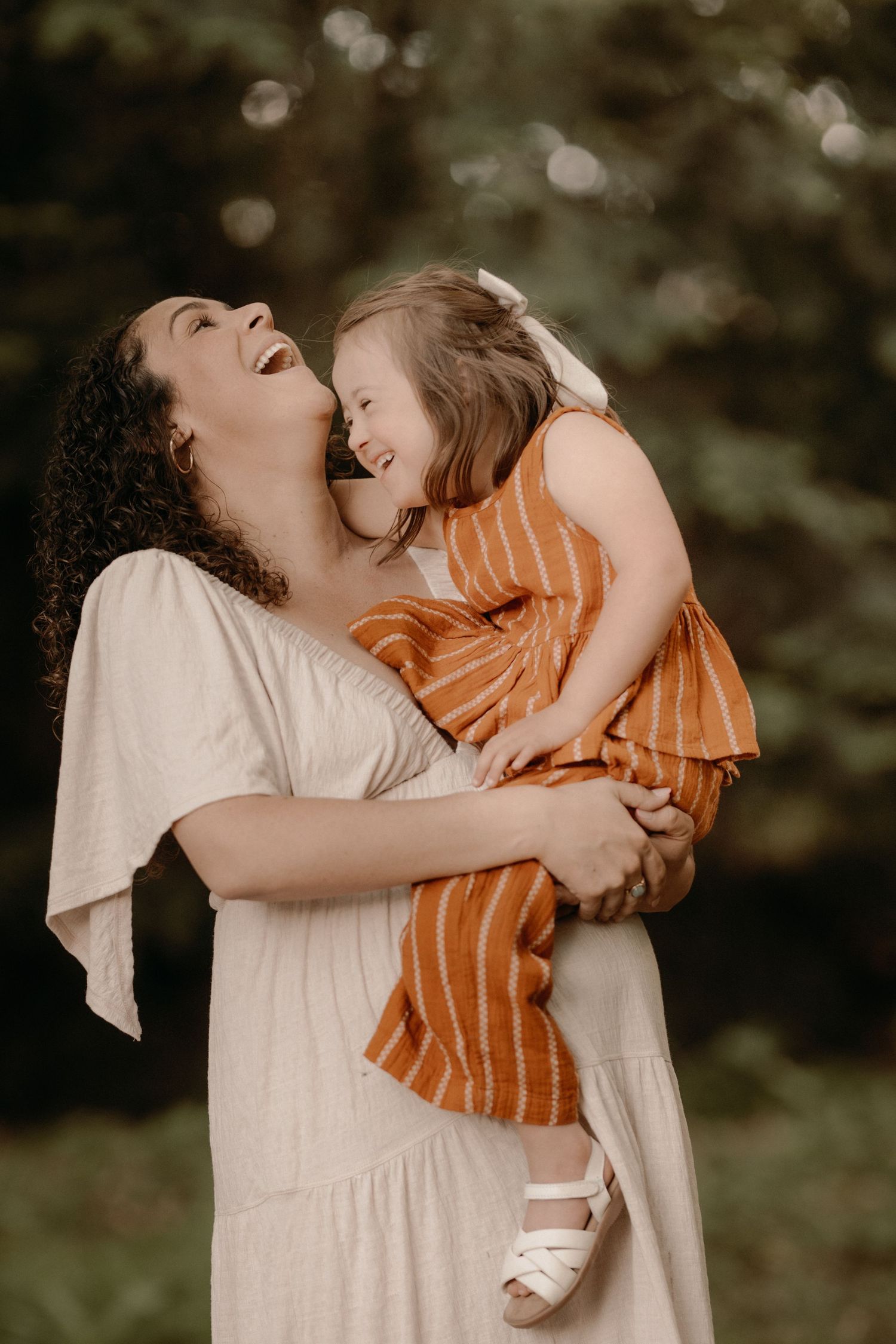 Mother laughs joyfully while holding her daughter in a tender outdoor motherhood portrait.