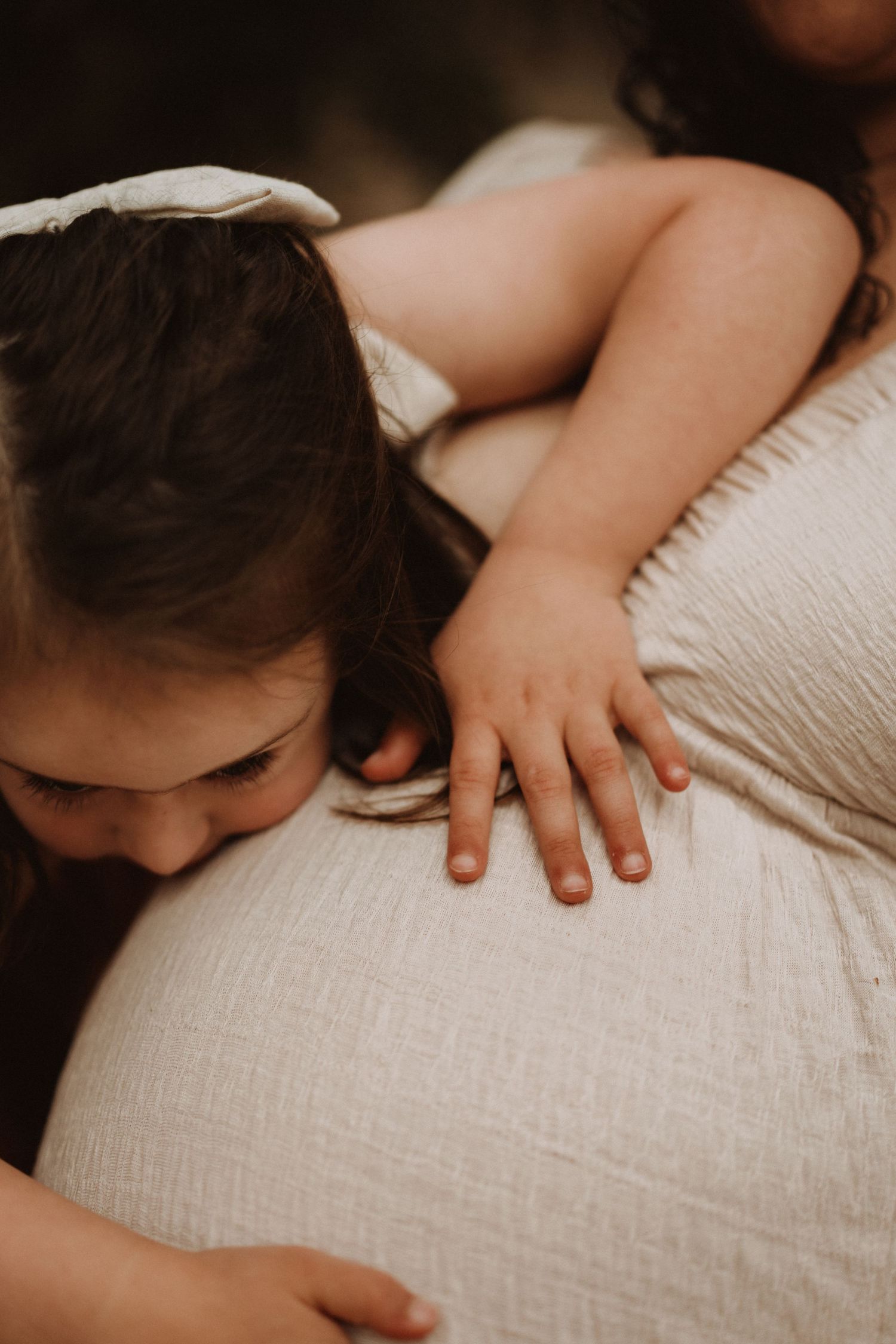 Child hugs her mother’s pregnant belly in a heartfelt, emotional maternity portrait.
