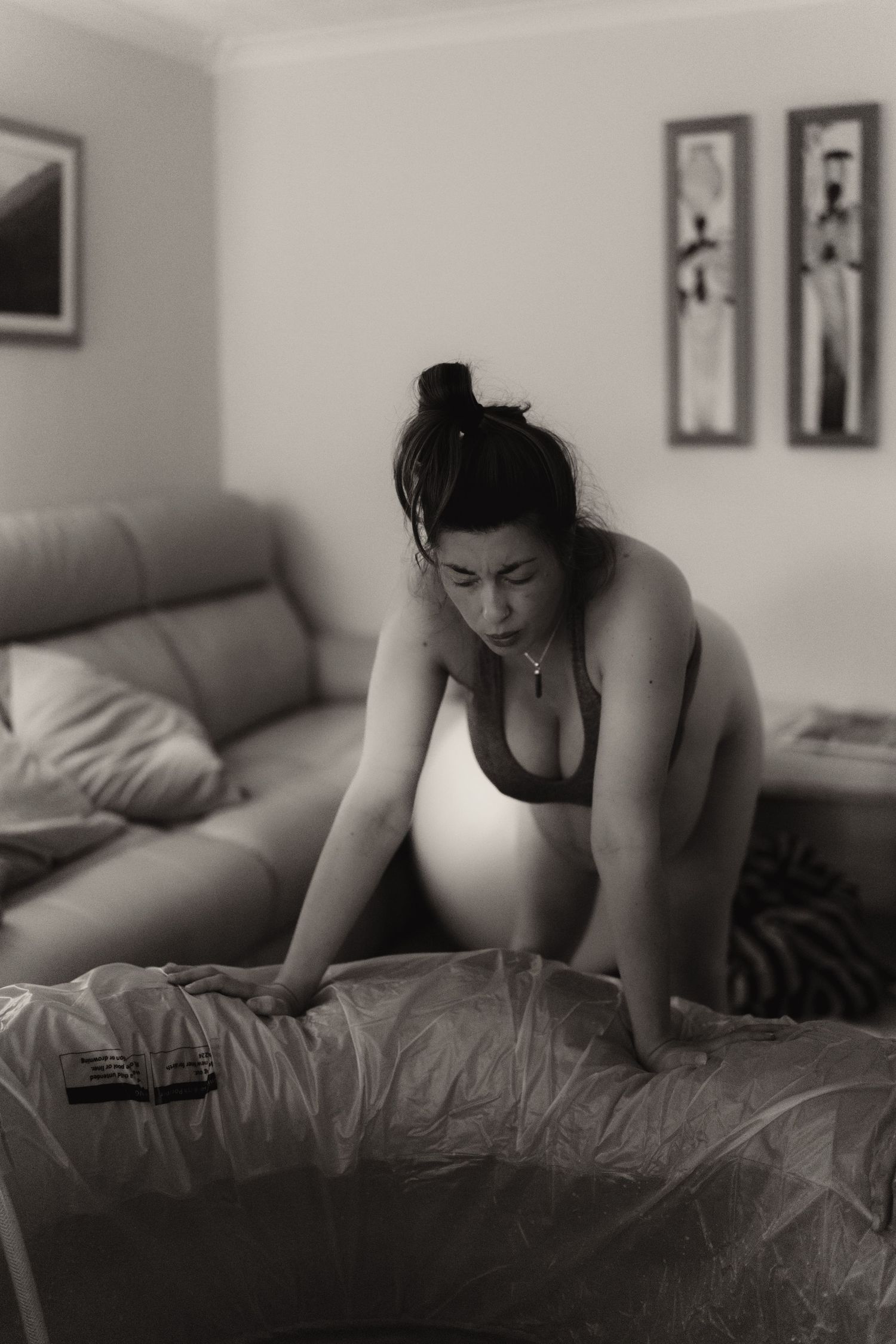Pregnant parent leaning forward during early labour at home, documented in a natural birth photography session.