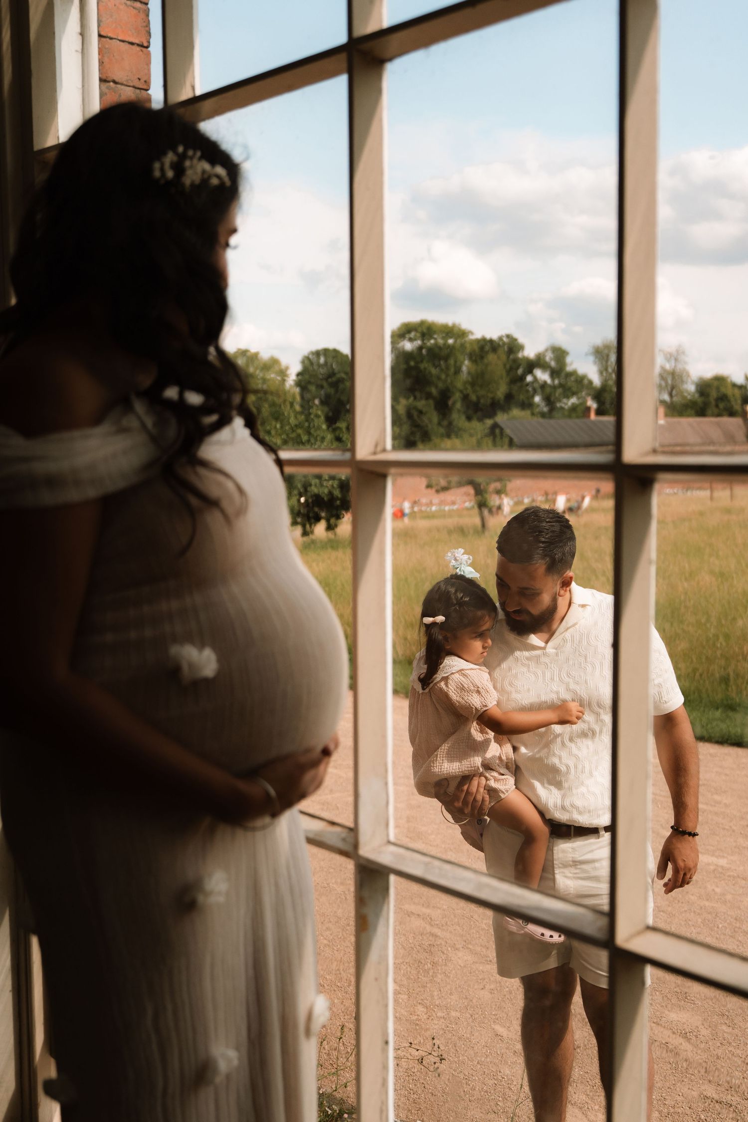 Couple embraces by a large window as sunlight pours in, capturing the calm before welcoming a new baby.