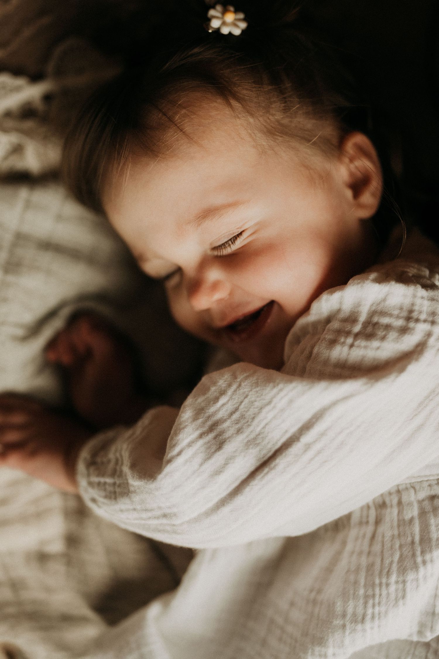 miling newborn lying on a bed in natural light during an in-home lifestyle newborn photography session.