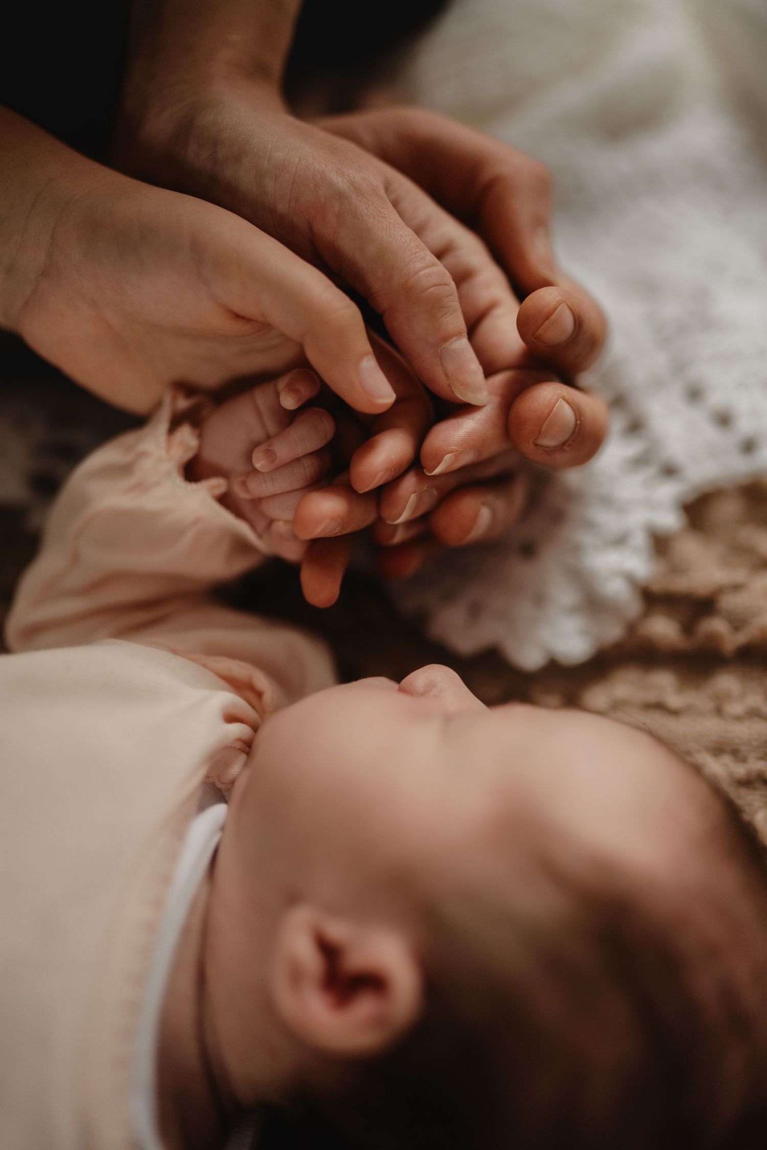 Parent gently holding a newborn’s tiny hands in an intimate storytelling photoshoot at home in Swadlincote