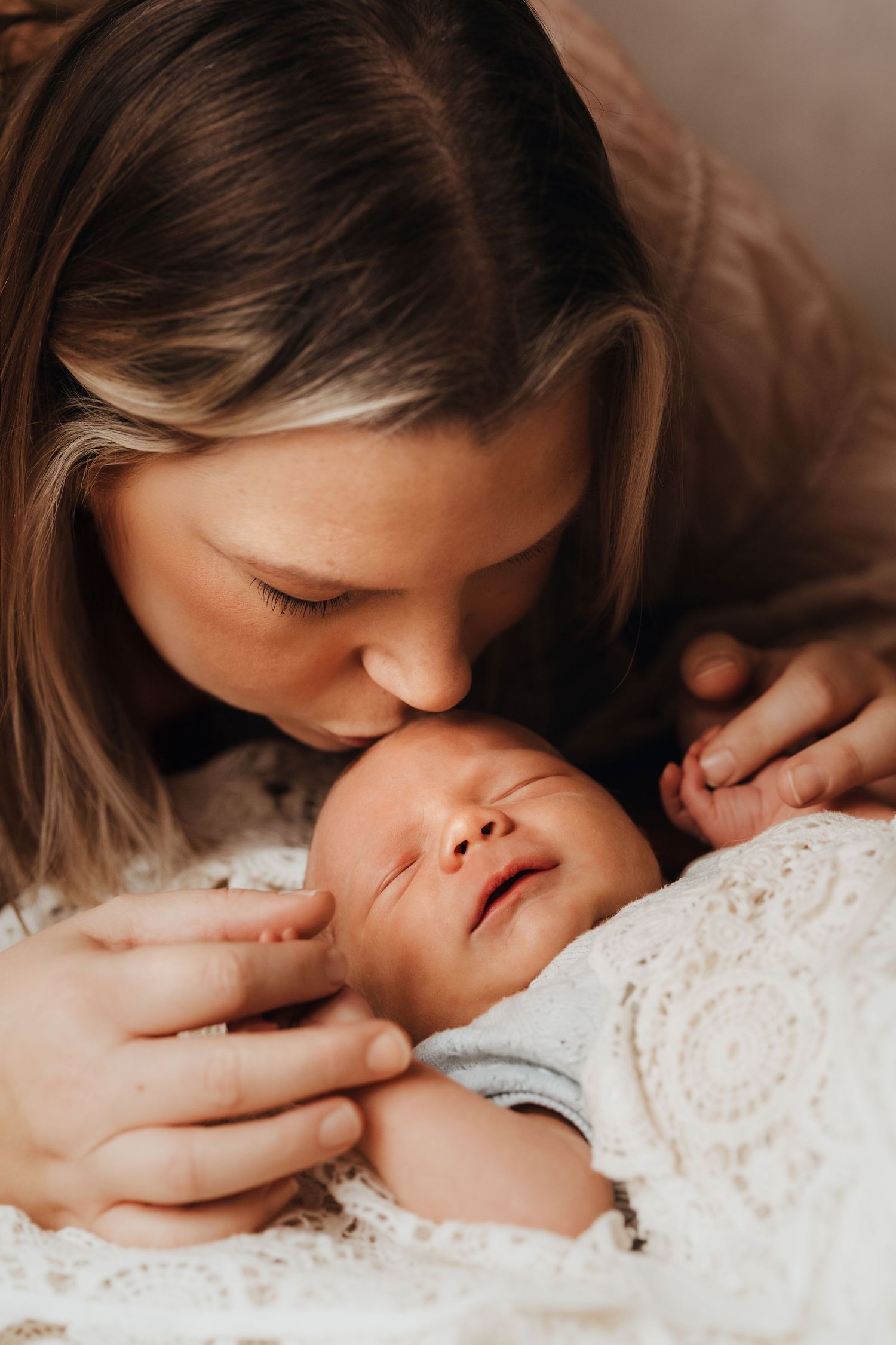 Mother kissing her newborn’s head during a warm natural light lifestyle newborn photography session.