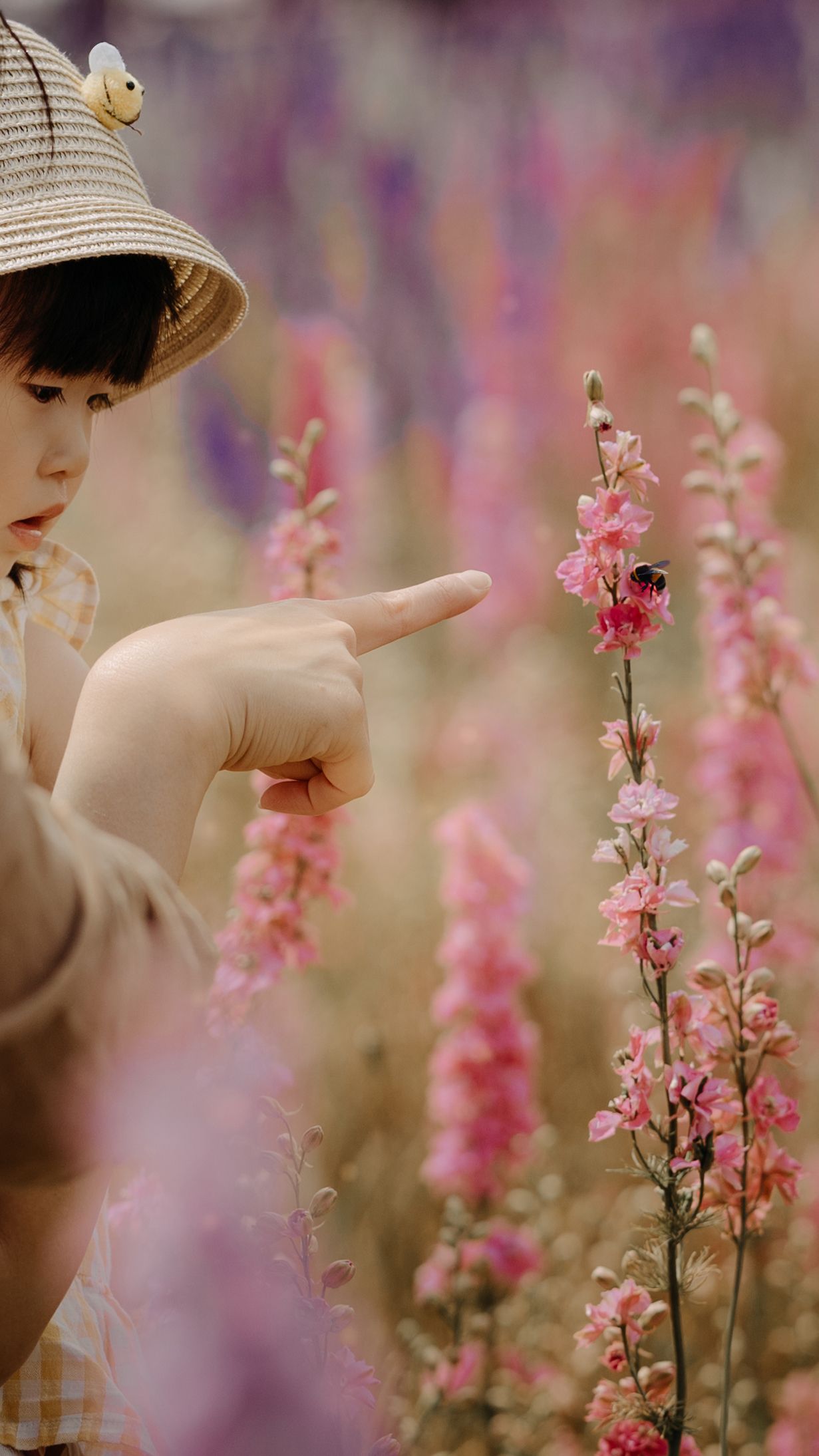 little girl watching a bumble bee siting on delphinium flower in real flower petal confetti