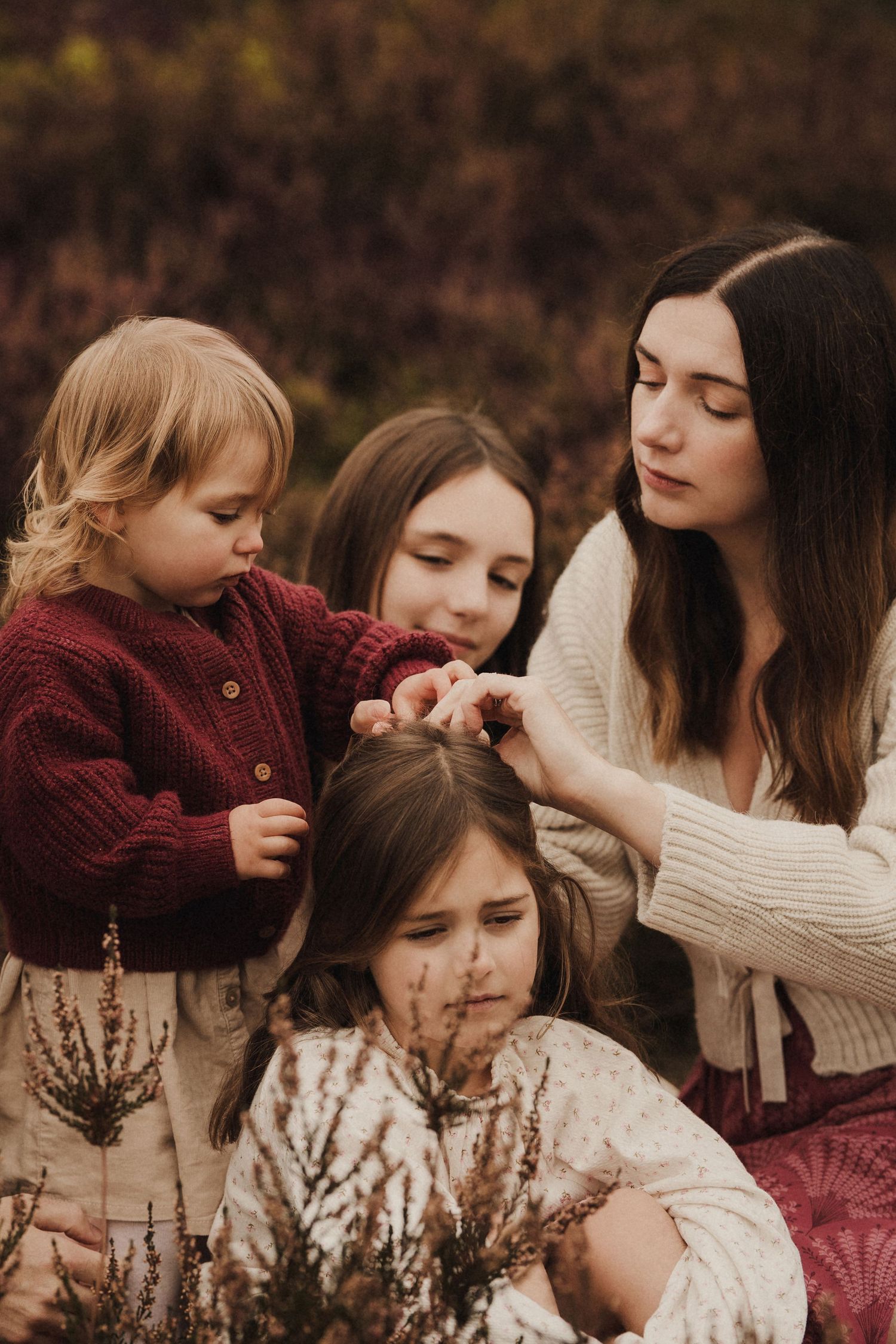 Mother sitting with her children outdoors, gently adjusting hair during a calm, storytelling family photoshoot in Birmingham