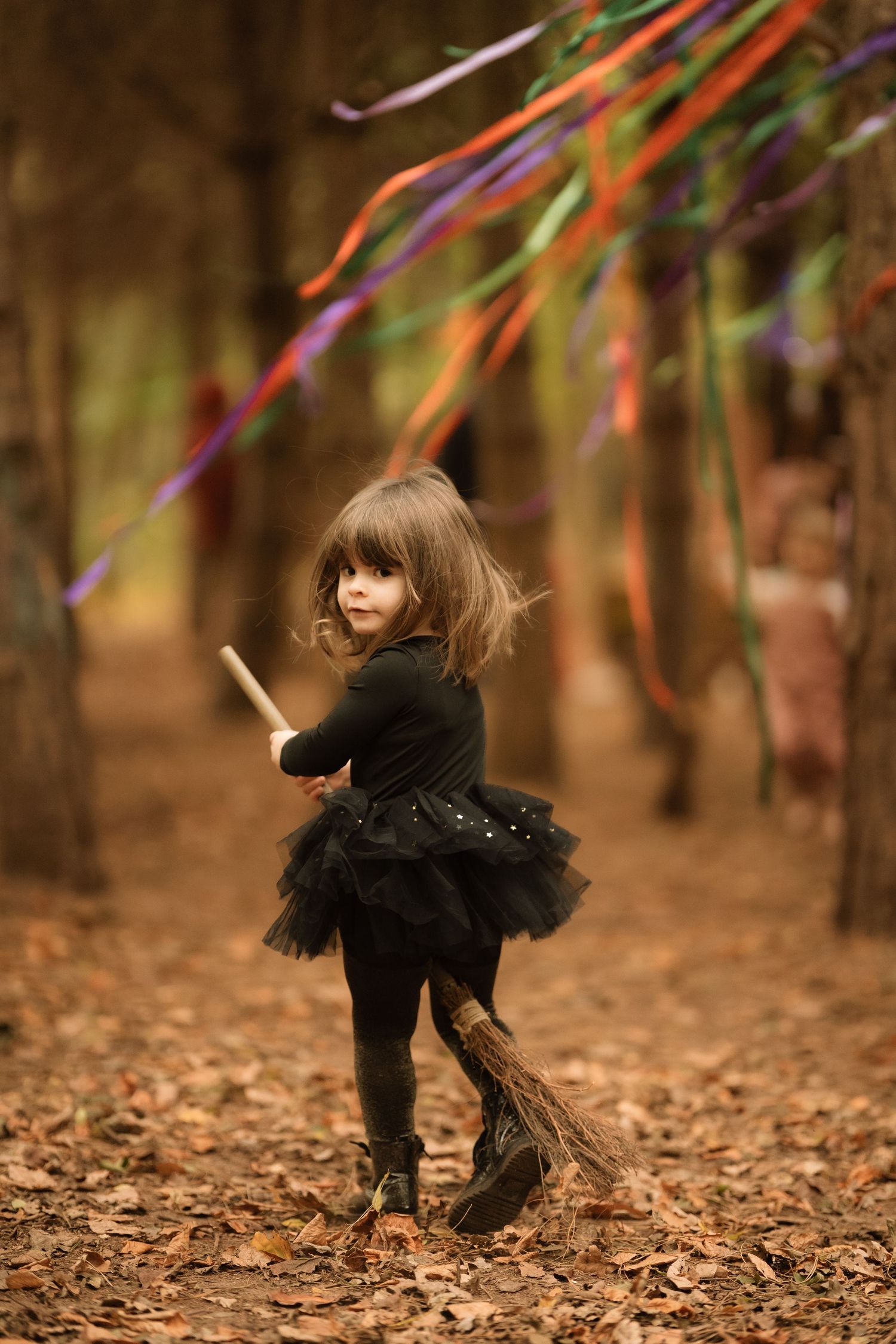 Child in black tutu runs through forest ribbons during a playful storytelling photoshoot outdoors at Little Wildlings natureplay