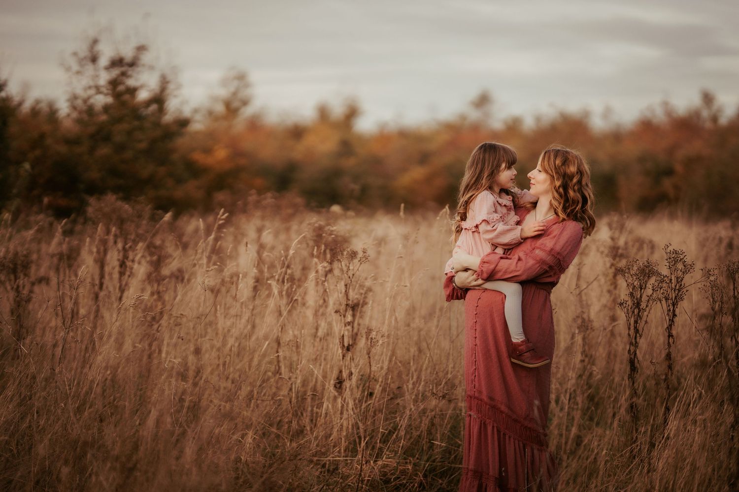 Expectant mother holding her daughter in her arms in an autumnal field in Coalville