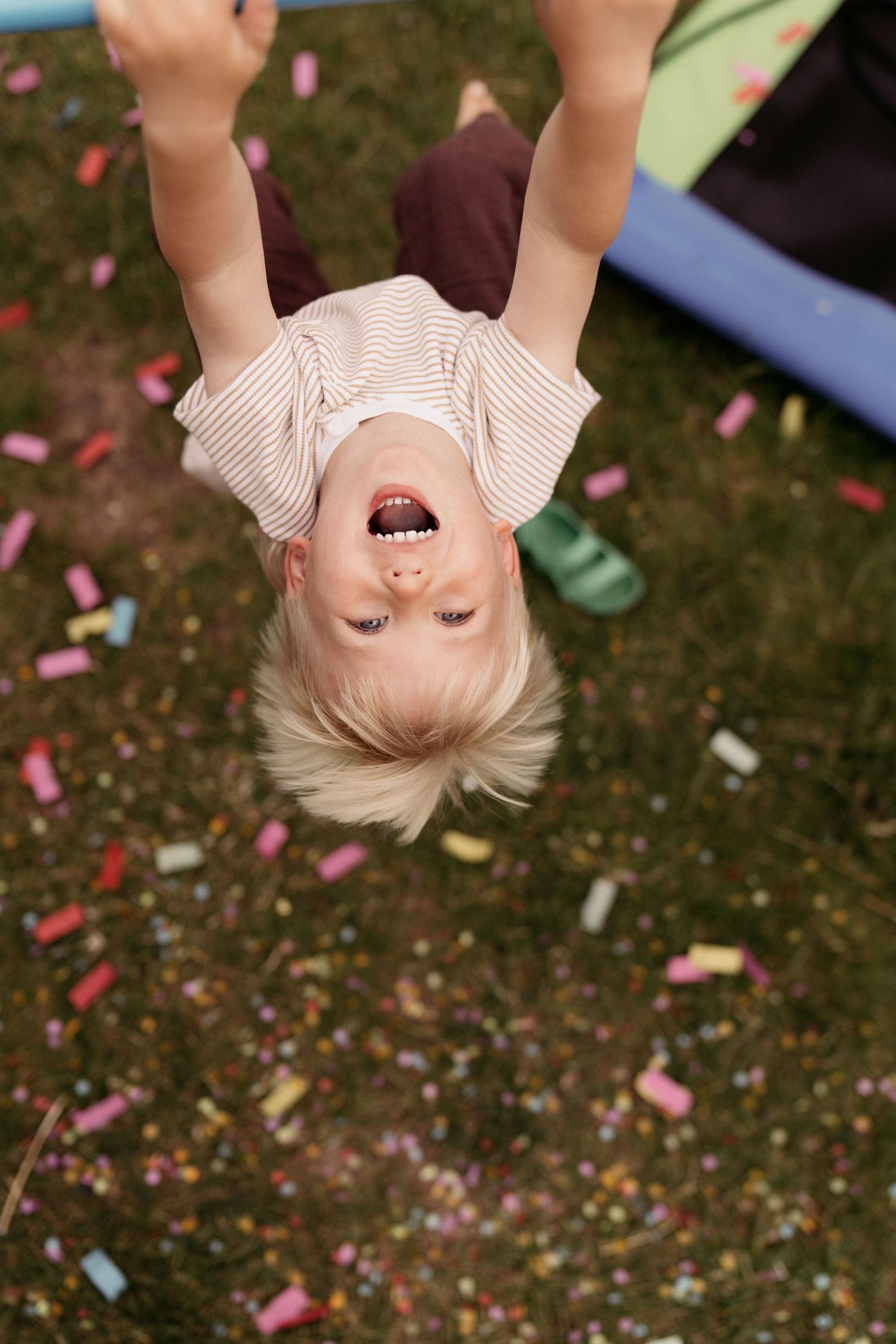 A child hangs upside down laughing, arms stretched wide as confetti scatters below, captured mid-play during a joyful family photoshoot.