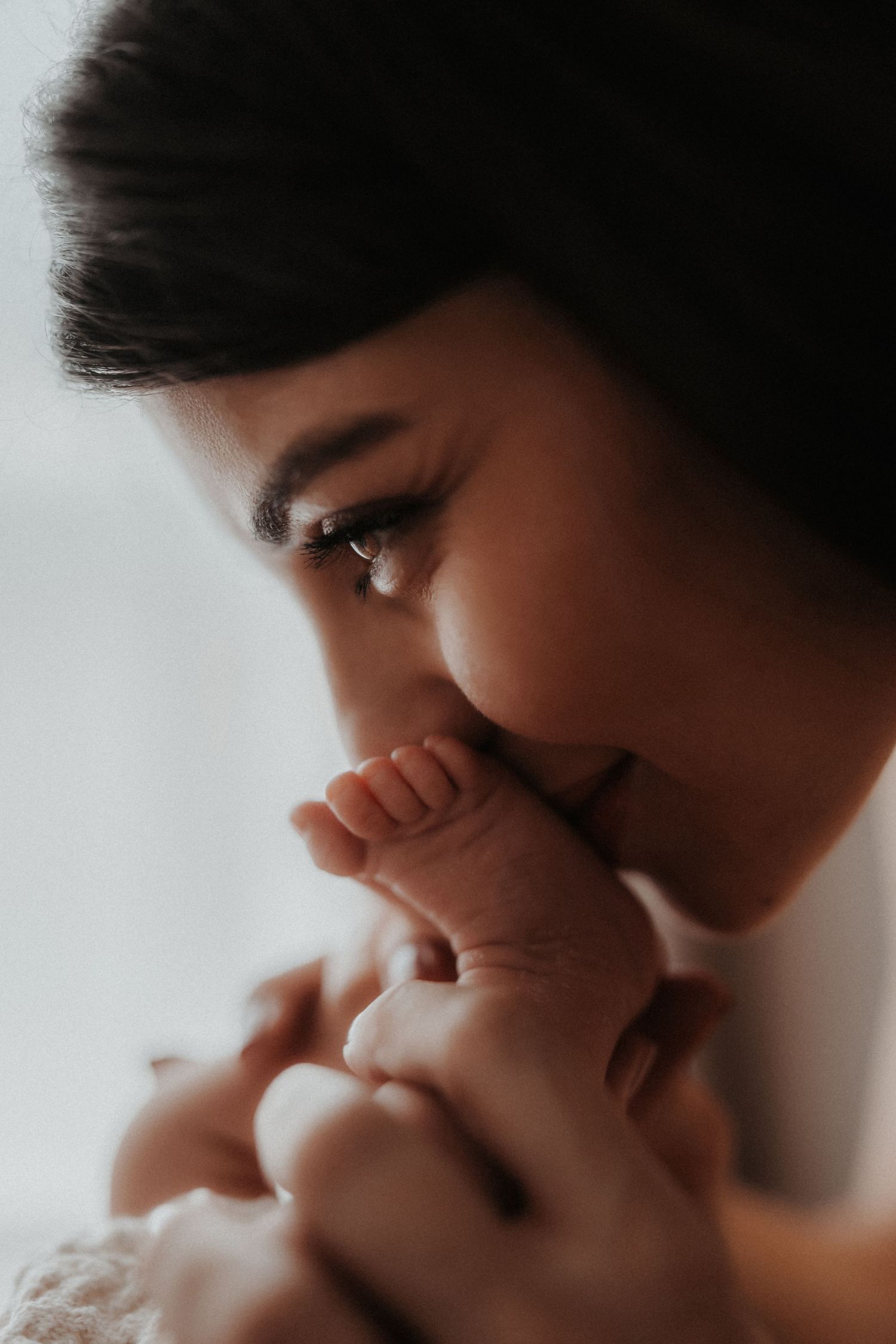 Mother kissing tiny baby feet during a soft storytelling newborn photoshoot in window light. macro newborn shoot