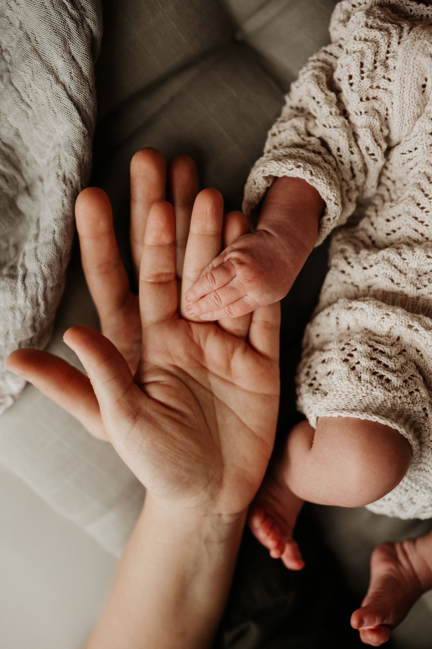 Newborn’s tiny hand resting against a parent’s palm, a quiet detail photographed during a natural storytelling photoshoot.