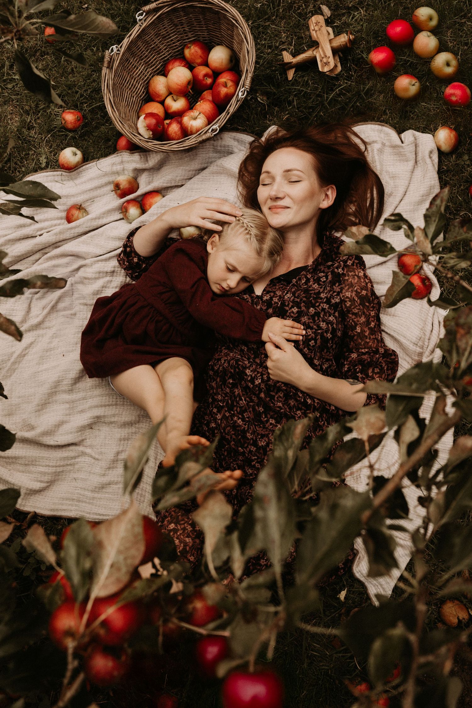 Family photoshoot, Angela on a picnic blanket in an orchard, surrounded by apples, resting together with her daughter