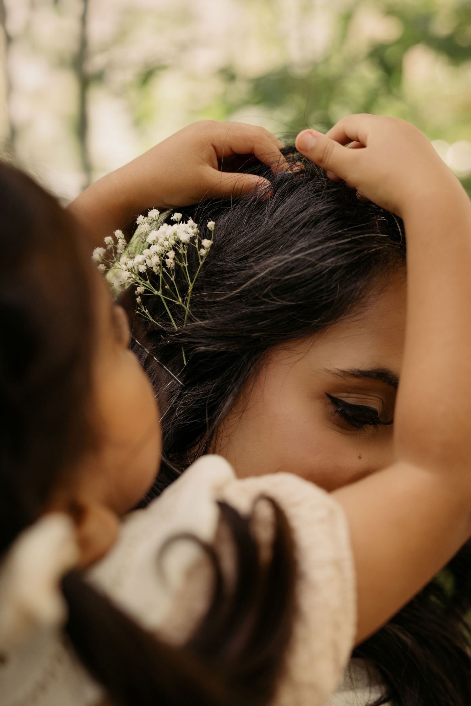 Mother hugging her child outdoors during a natural light lifestyle family photography session. Daughter placing a flower in mums hair