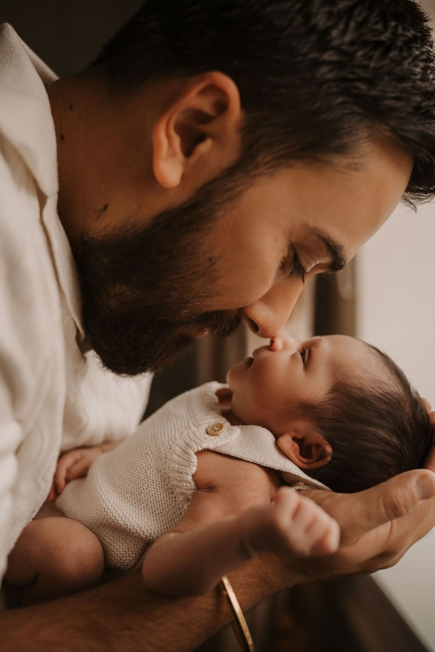 Father kissing his newborn during a tender lifestyle newborn photoshoot at home in soft window light.